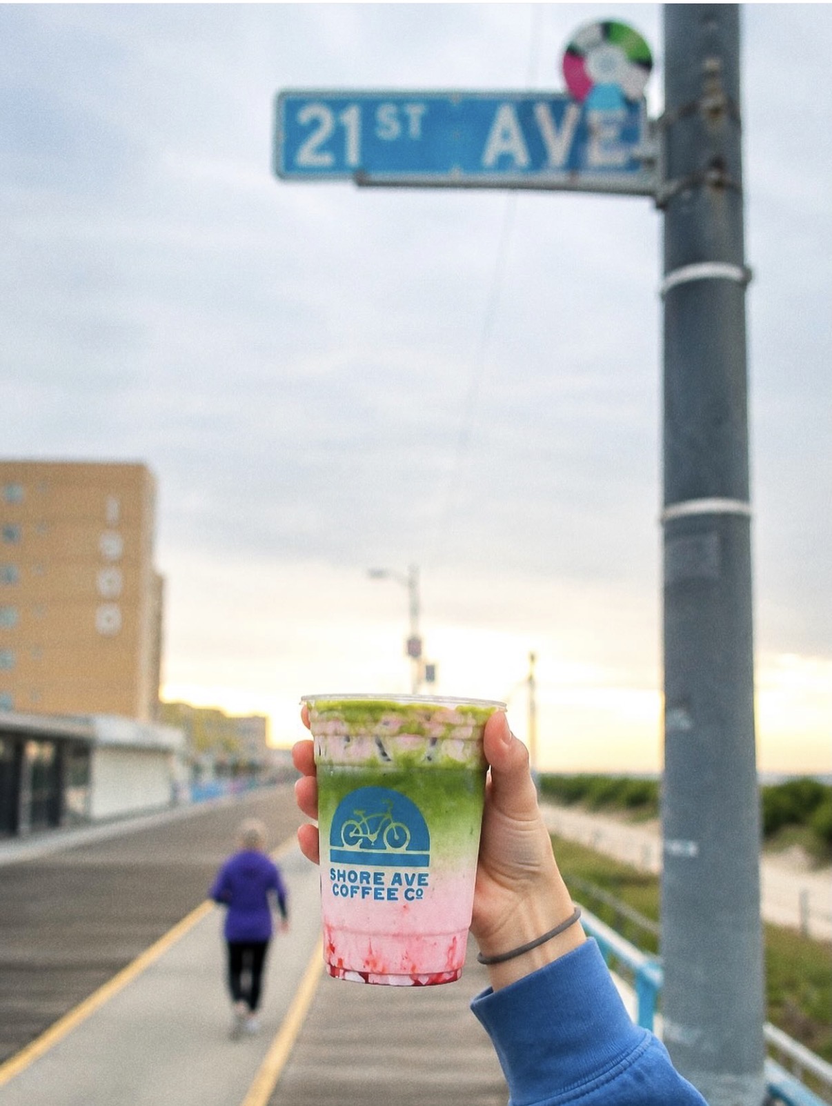 Person holding a colorful drink with a street sign reading 21st Avenue in the background.