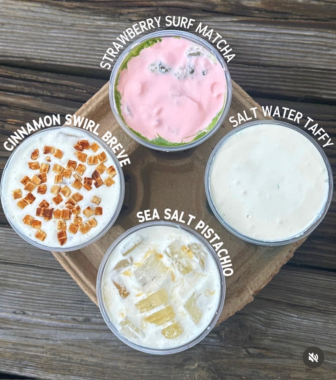 Four drinks in clear cups with labels: strawberry surf matcha, salt water taffy, sea salt pistachio, cinnamon swirl brew, on a wooden surface.