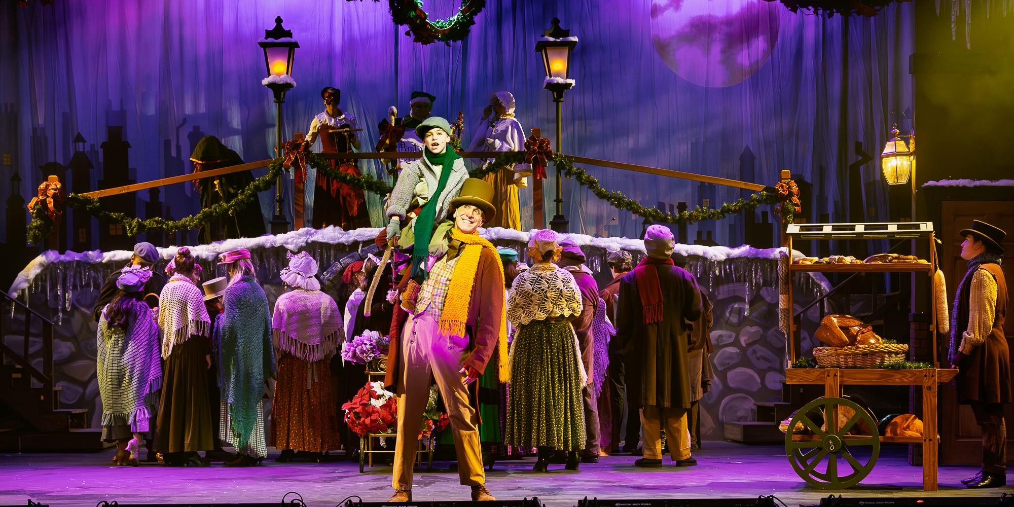 Theatrical stage scene with actors in colorful costumes, some with umbrellas, and a decorated backdrop with purple lighting.