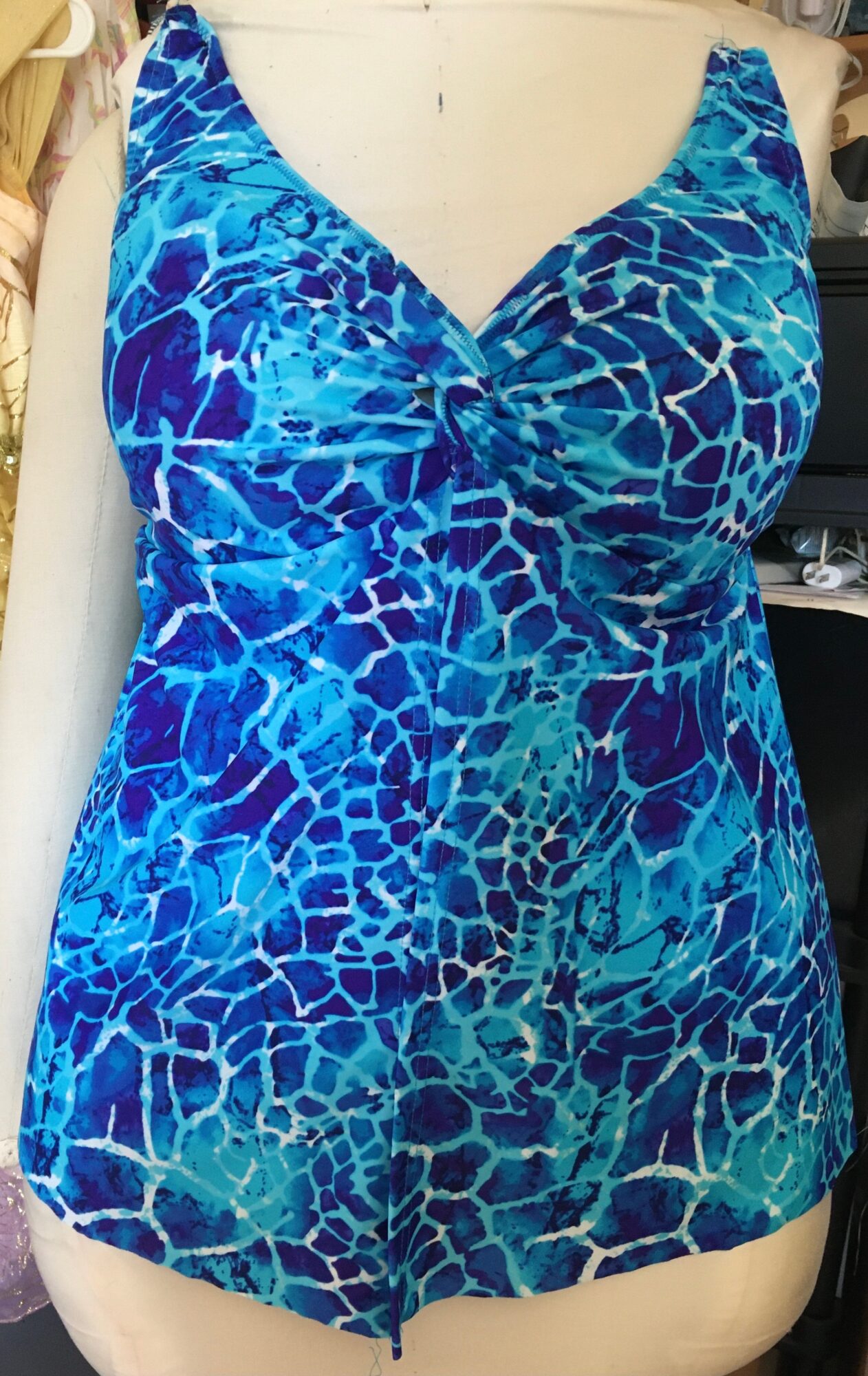 Blue patterned sleeveless top with a V-neck, displayed on a mannequin, with a mosaic-like design.