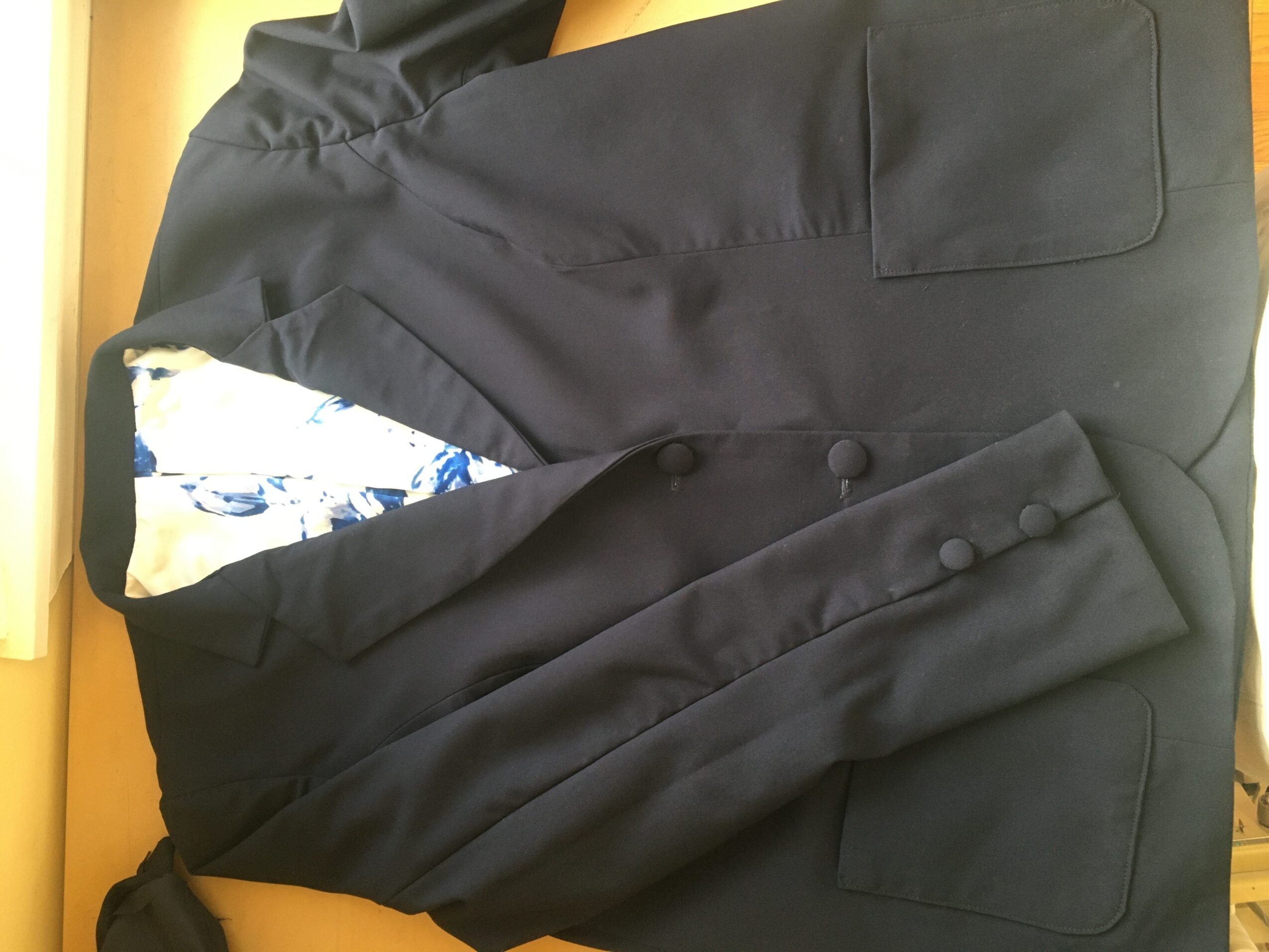 Black blazer with a floral inner lining, hanging on a hook or hanger, viewed from the side.