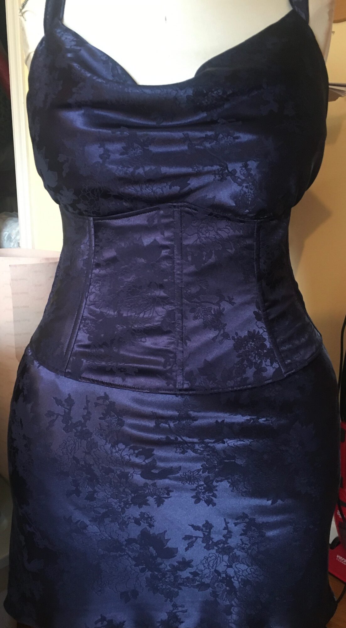 Person wearing a dark, patterned, fitted dress with a structured bodice and a high waistline.