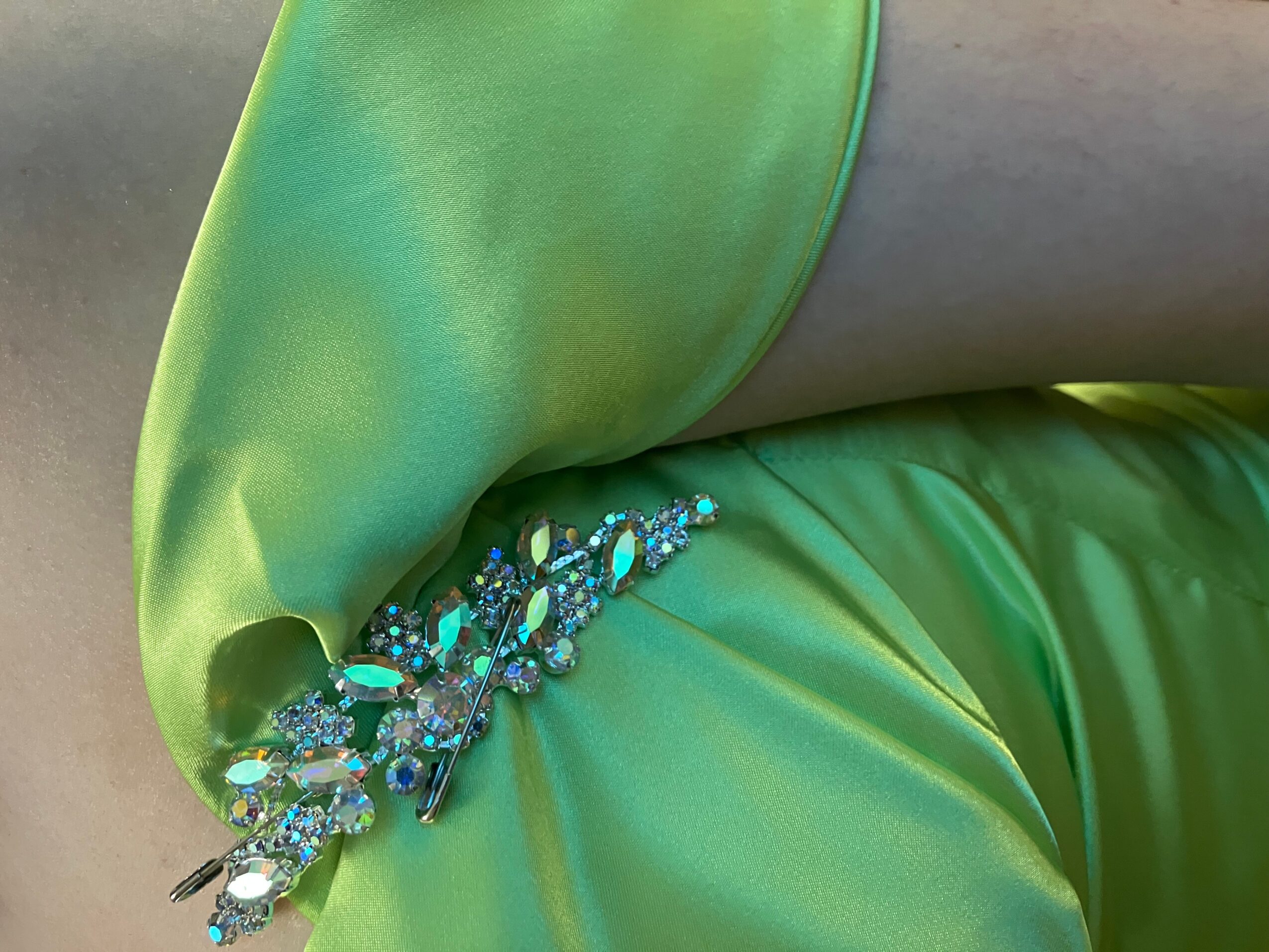 Close-up of a person wearing a bright green satin dress with a decorative beaded embellishment at the waist.