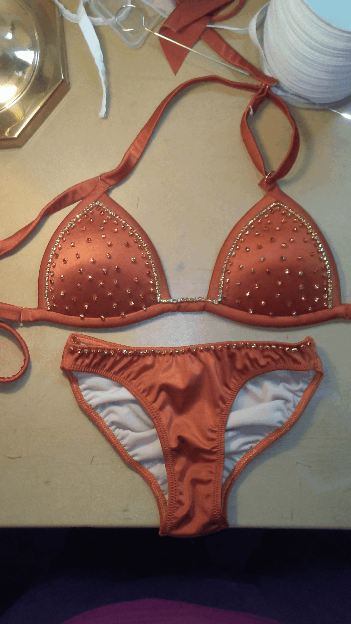 Orange bikini with studded embellishments on the top and ruffled bottom, laid on a light-colored surface.