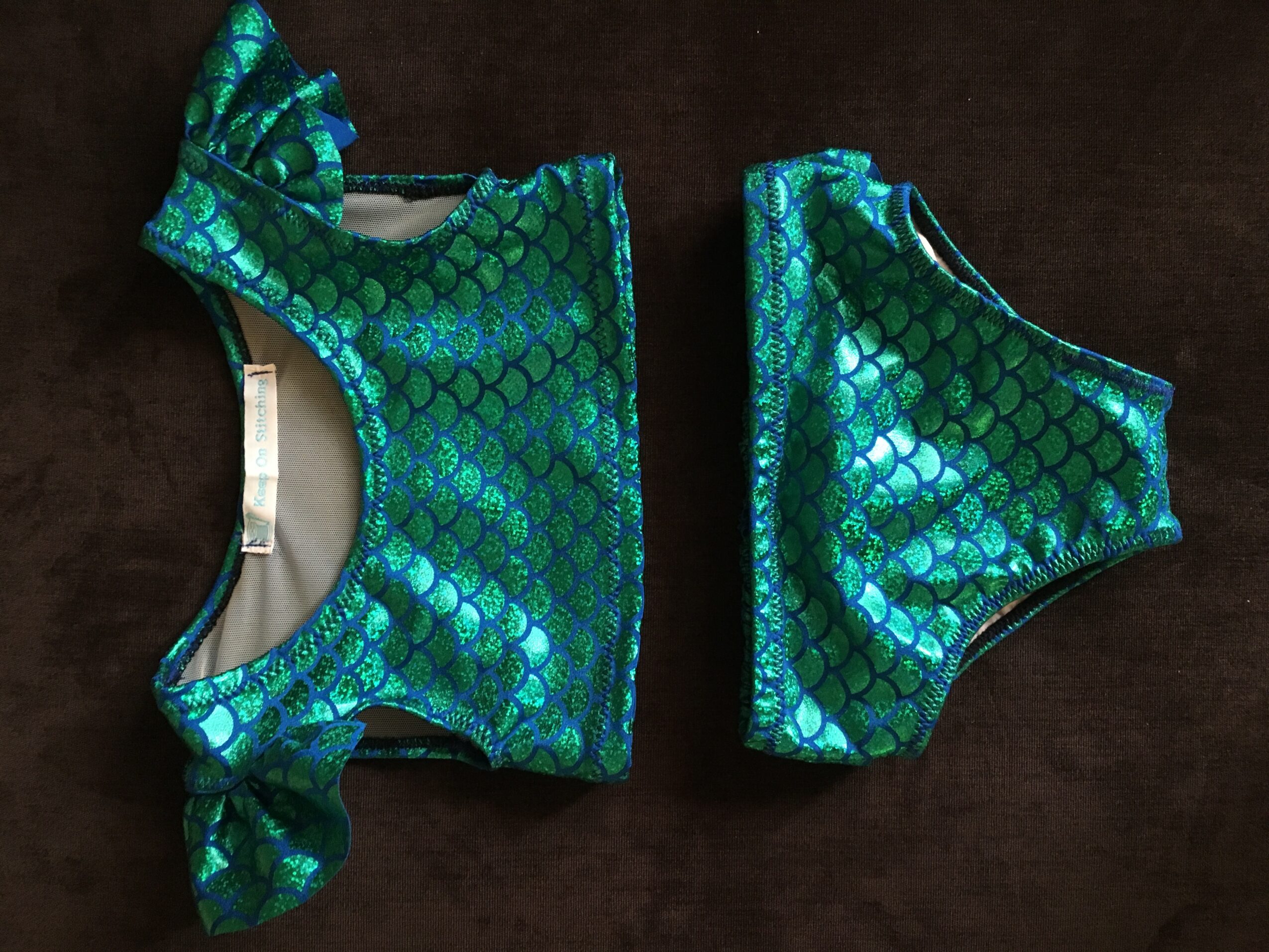 Two pieces of clothing with a shiny, green, fish-scale pattern on a dark background.