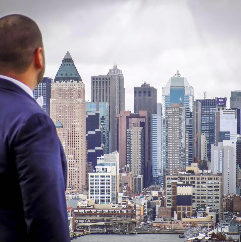 Man in suit looking at a city skyline with tall buildings under cloudy sky.