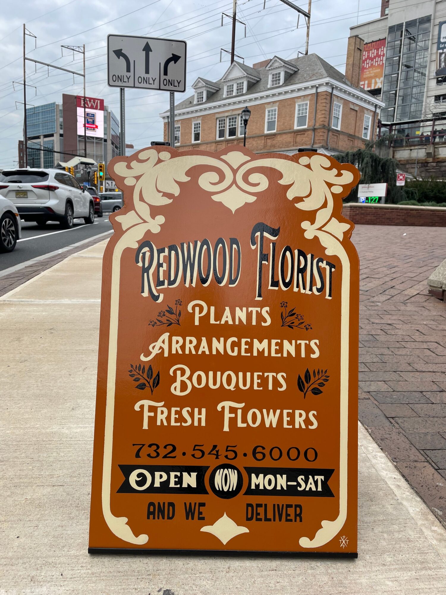 Signboard advertising local plant, arrangement, bouquet, and fresh flower deliveries, with contact details and opening hours.