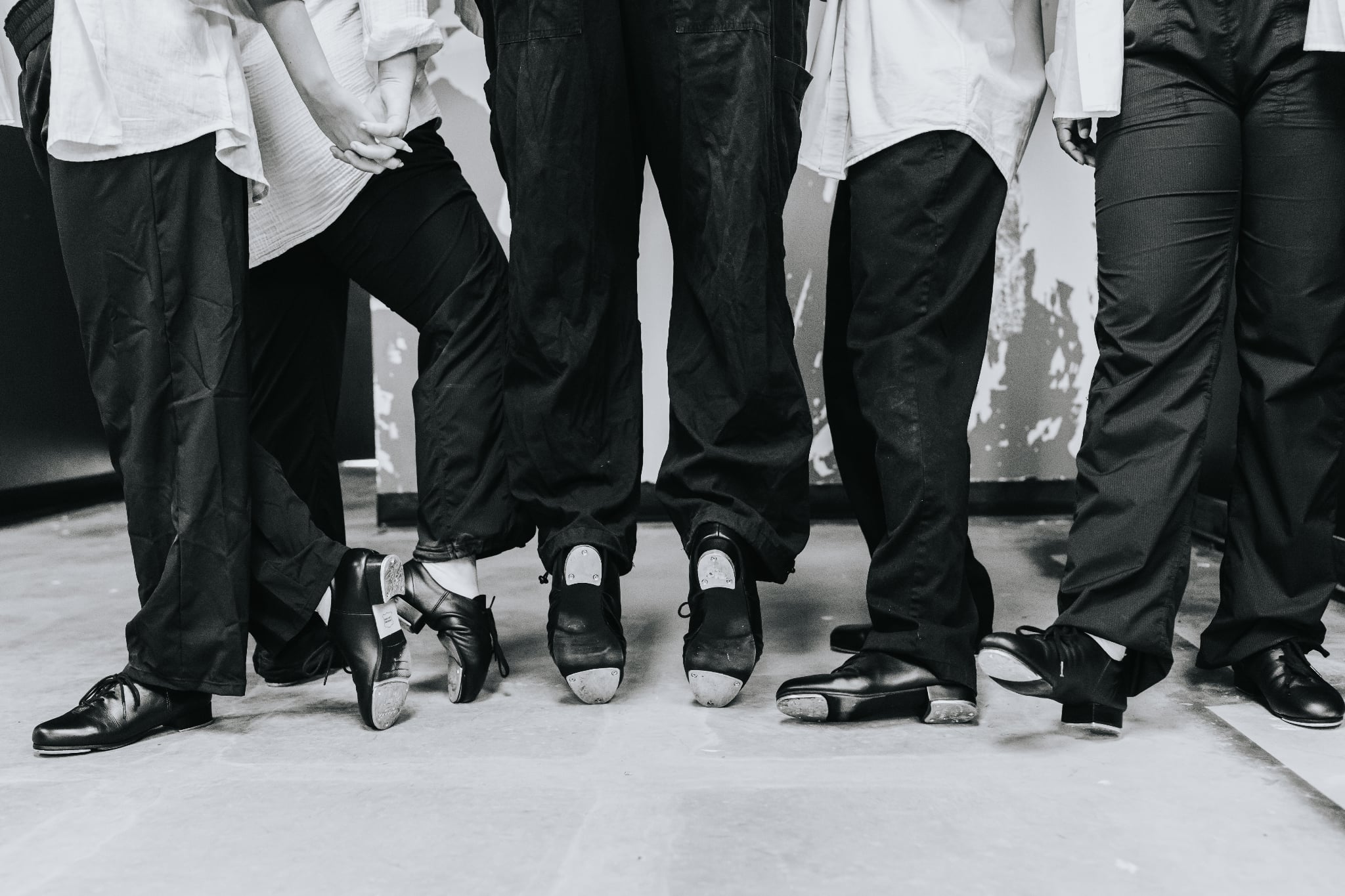 Six people standing in a row, showing their legs and feet, wearing black and white clothing and shoes.