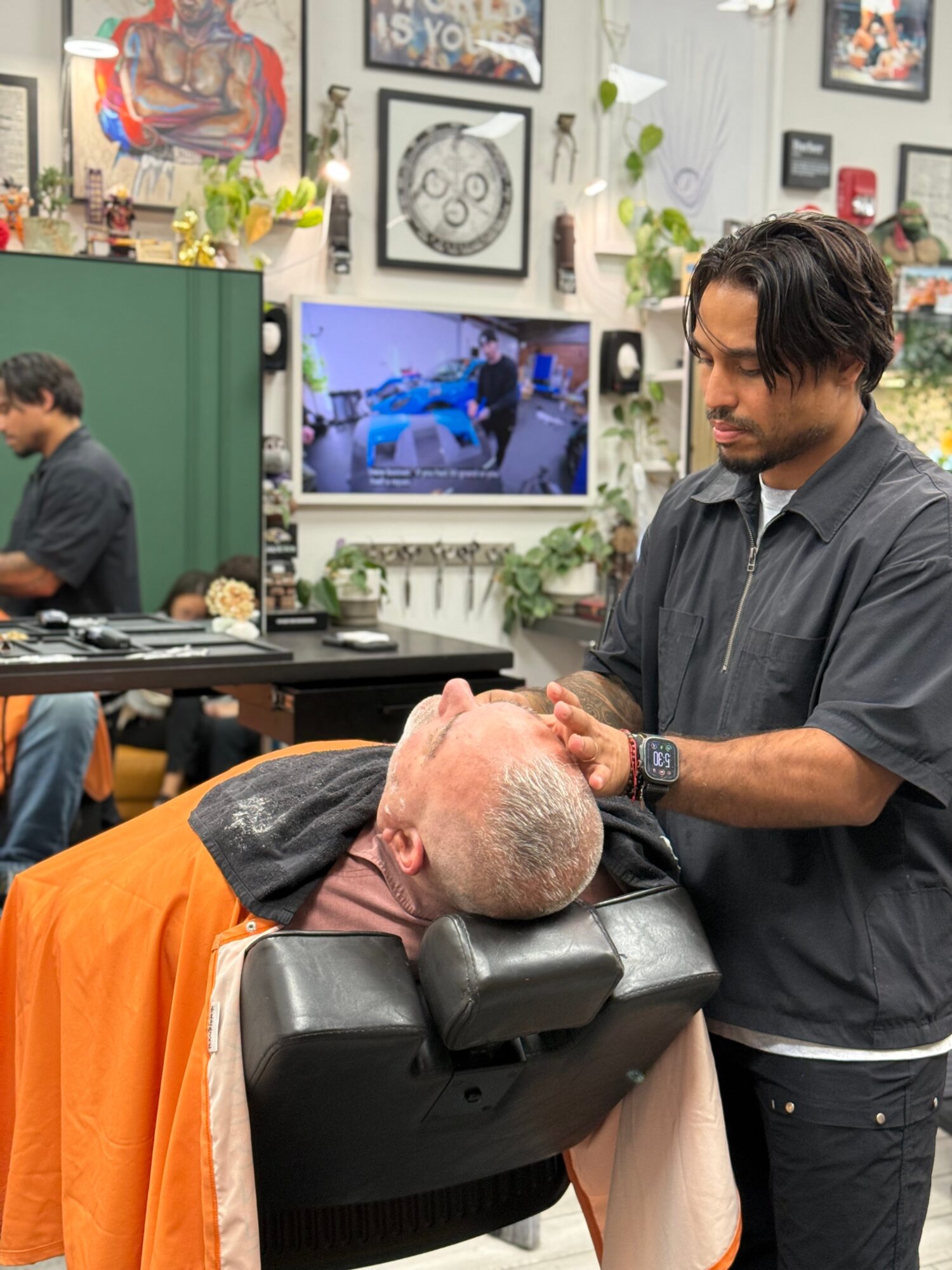 Barber cutting hair of a client lying back in a salon chair, with salon decor and artwork in background.