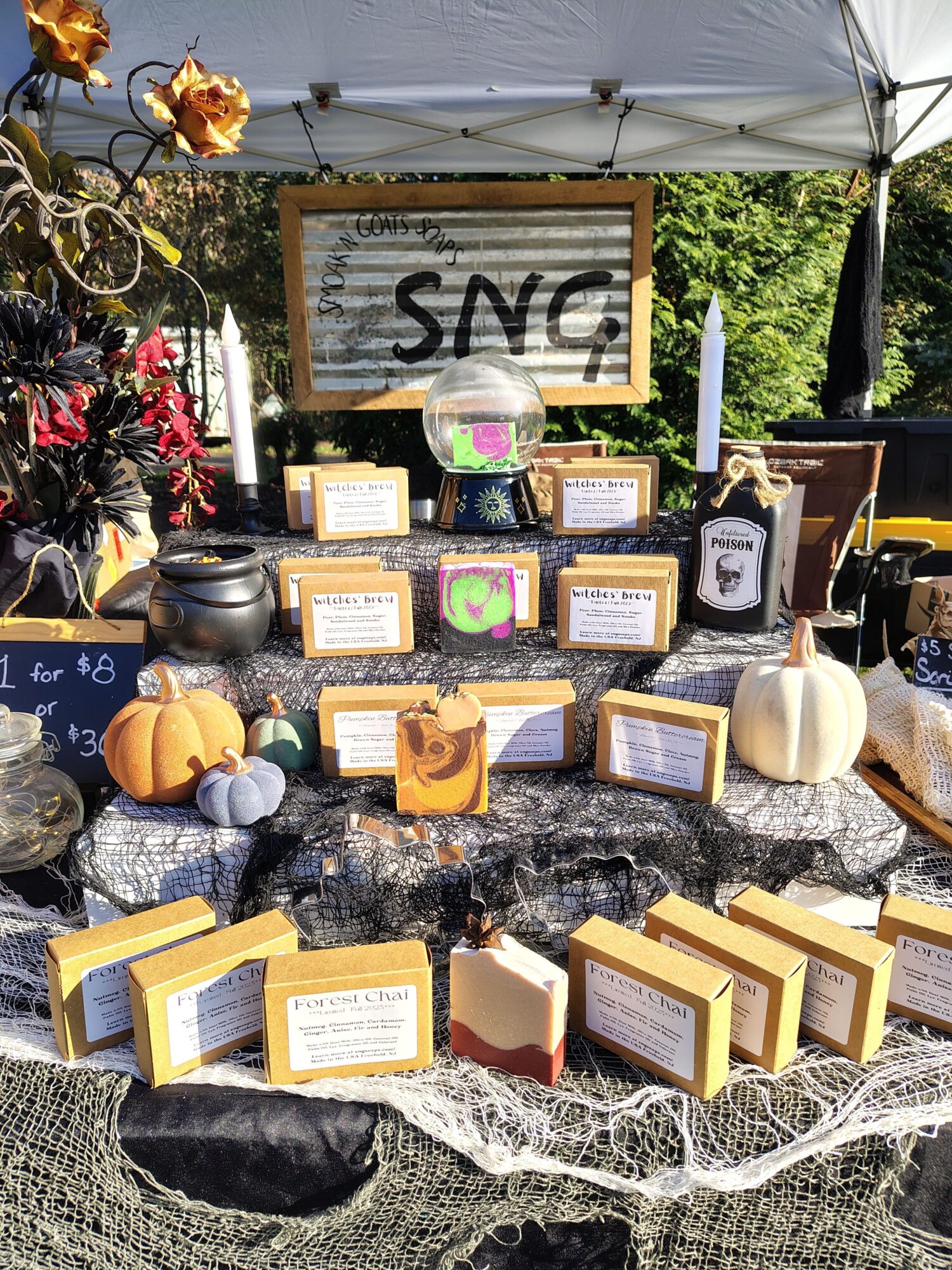 Display of framed photos, candles, and small pumpkins on a table outdoors, with a sign reading 'SNC' and decorative items.
