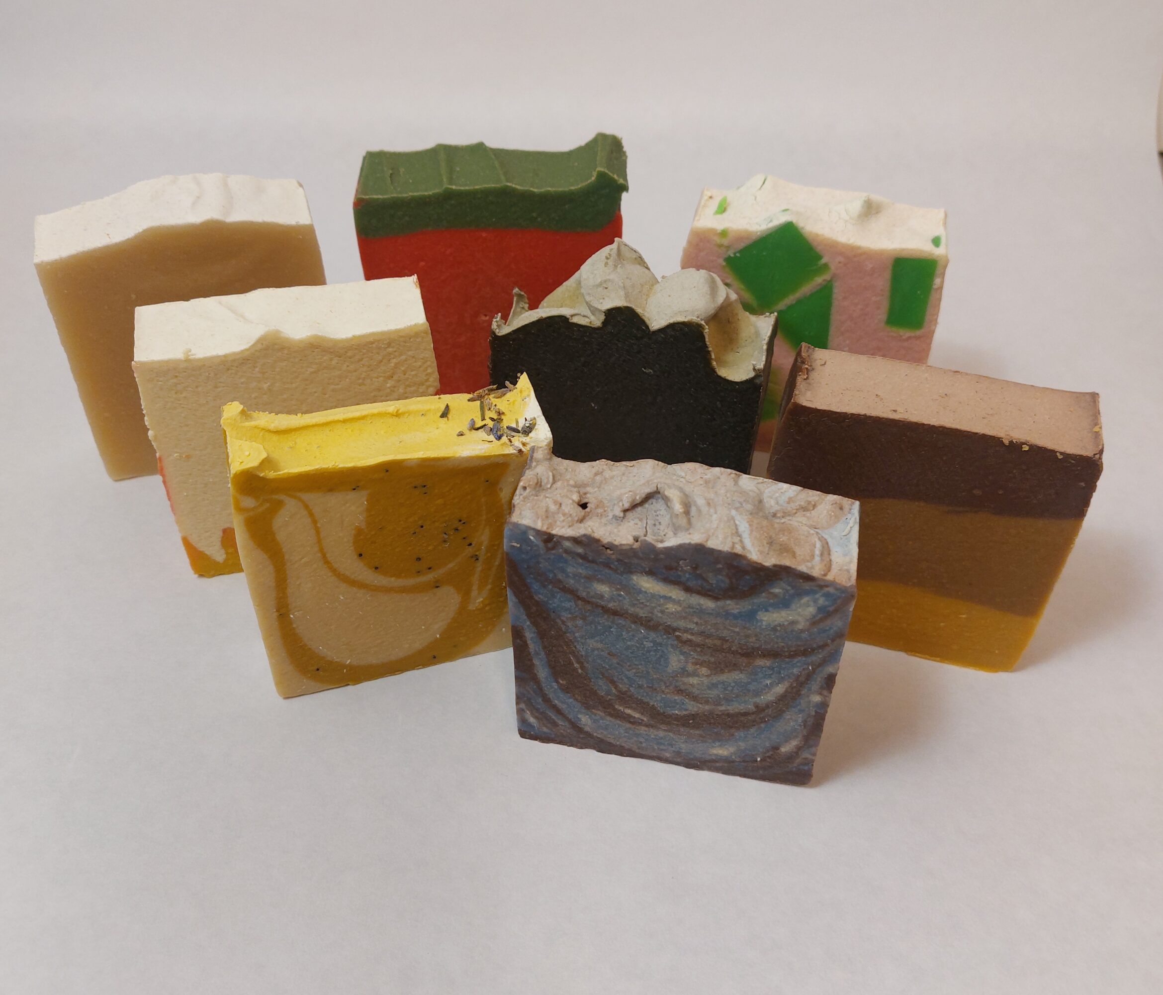 Nine colorful soap bars with various patterns and textures arranged on a white surface.
