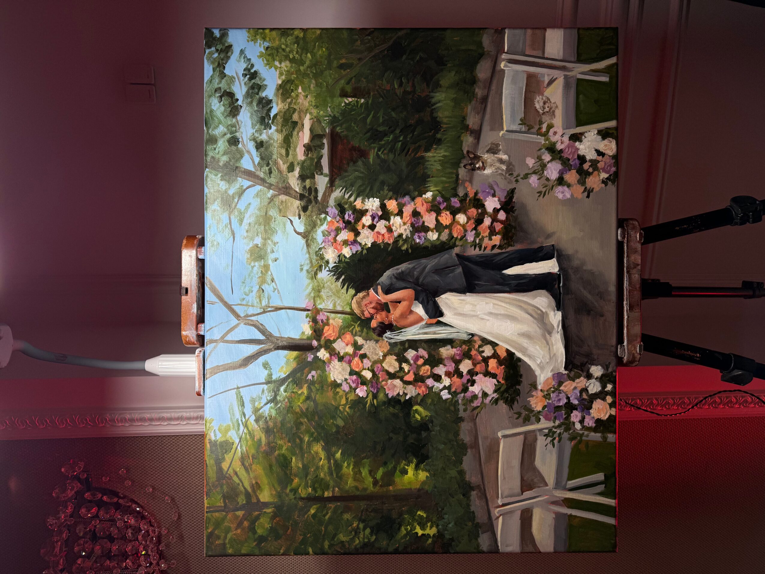 A woman in a white dress and black jacket stands outdoors near pink and white flowers, with trees and a pathway in the background.