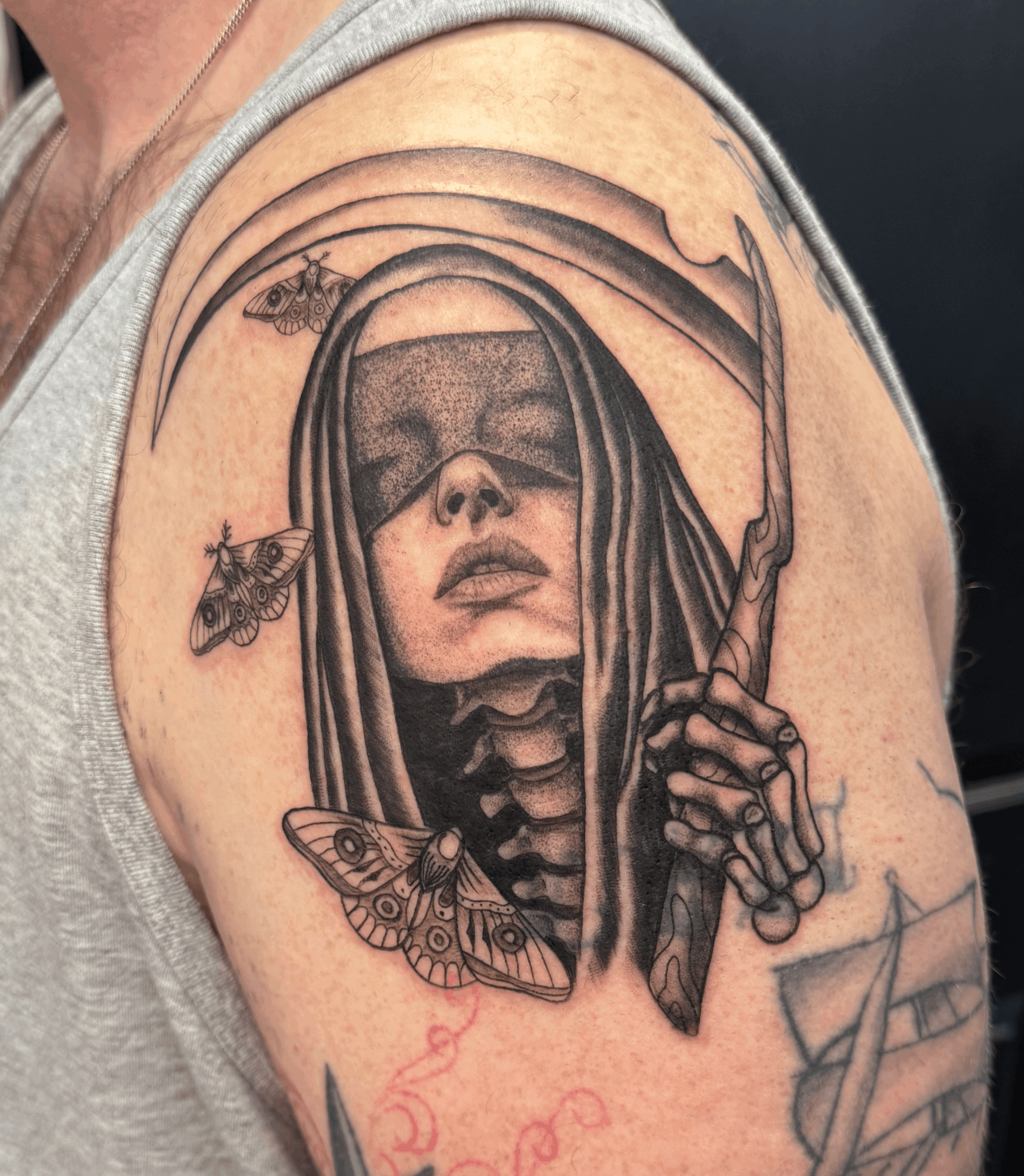 Tattoo of a woman with long hair, holding a knife, with a moth and a bee nearby, in black and gray ink.