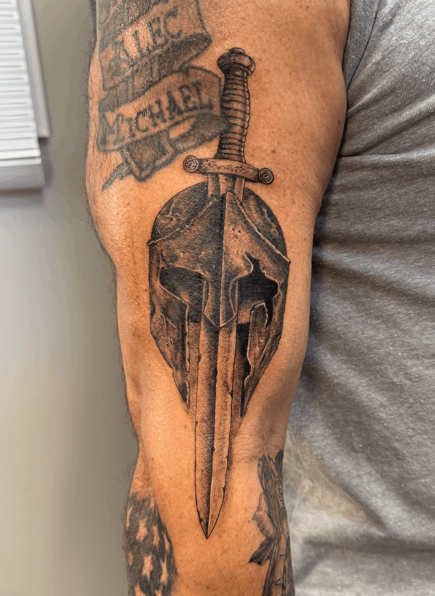 Tattoo of a sword piercing a skull on a person's arm, with additional tattoos visible nearby.