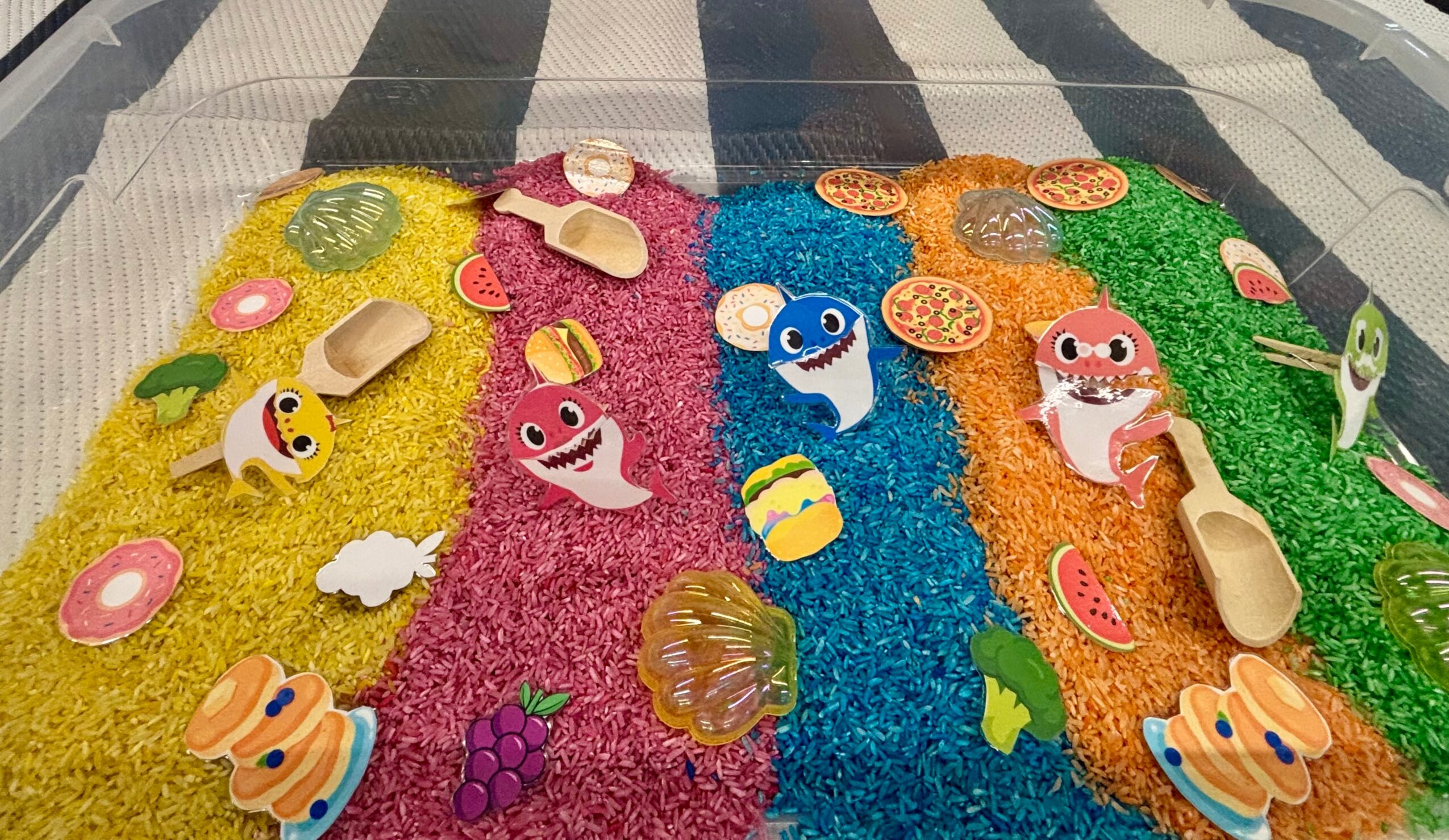 Colorful textured surface with small animal and fruit figurines, including a pink pig, blue whale, and yellow duck, arranged in rows.