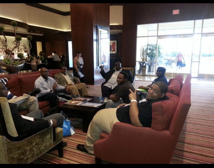 Group of people sitting and talking in a lobby area with large windows and a glass entrance door.