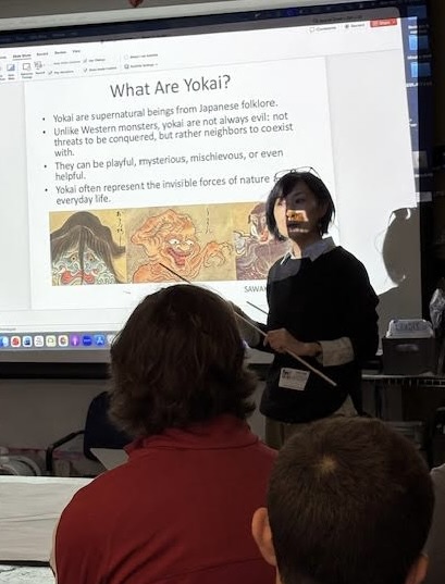 Person standing in front of a projected presentation slide, with audience members visible, discussing Yokai and their characteristics.