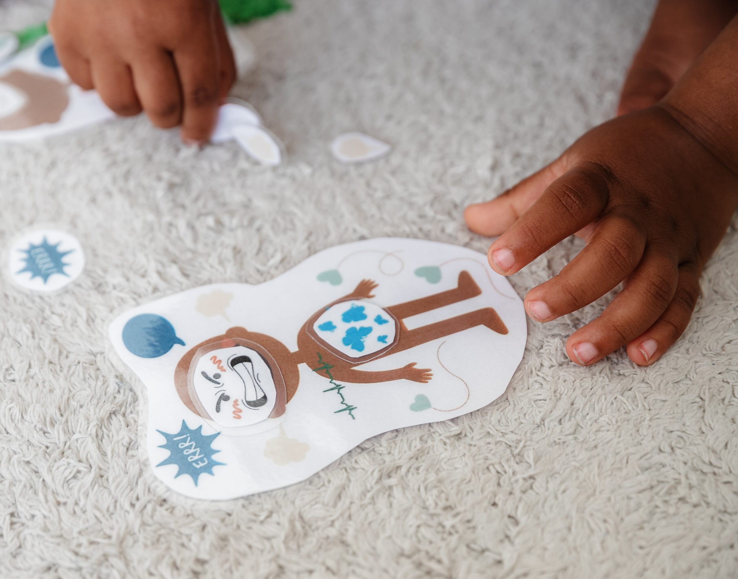 Two children play with a paper cutout of a person wearing a mask on a carpeted floor.