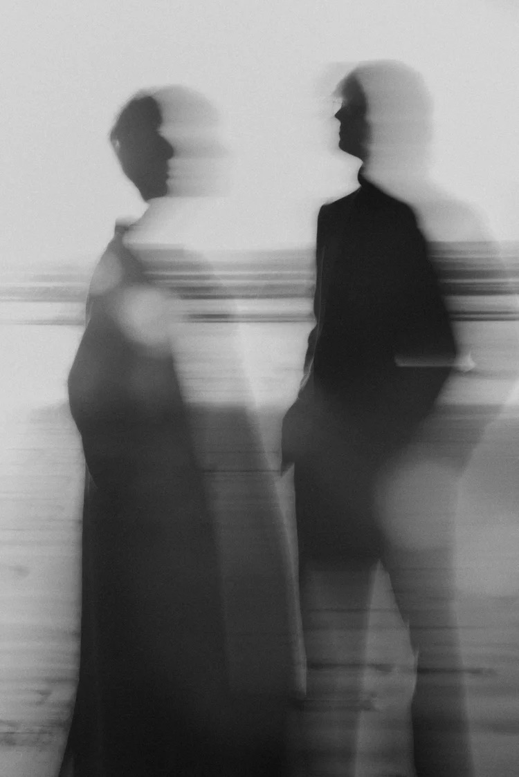 Two people standing and facing each other, with motion blur creating a distorted effect, in black and white.