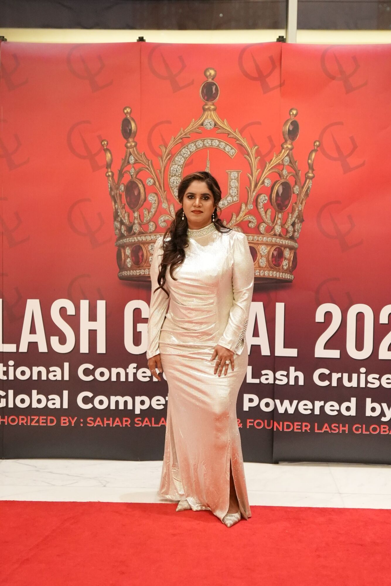 Woman in a pink gown standing in front of a red event backdrop with text and graphics.