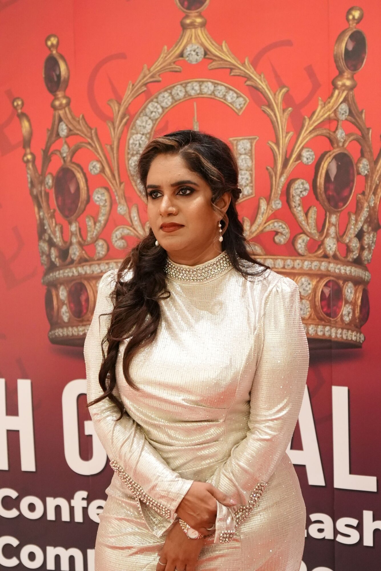 Woman in white dress with long dark hair, standing in front of ornate red and gold backdrop.