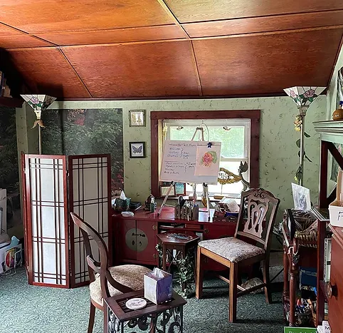 Room with green walls, wooden ceiling, window, chairs, and decorative items, including a folding screen and a small table.