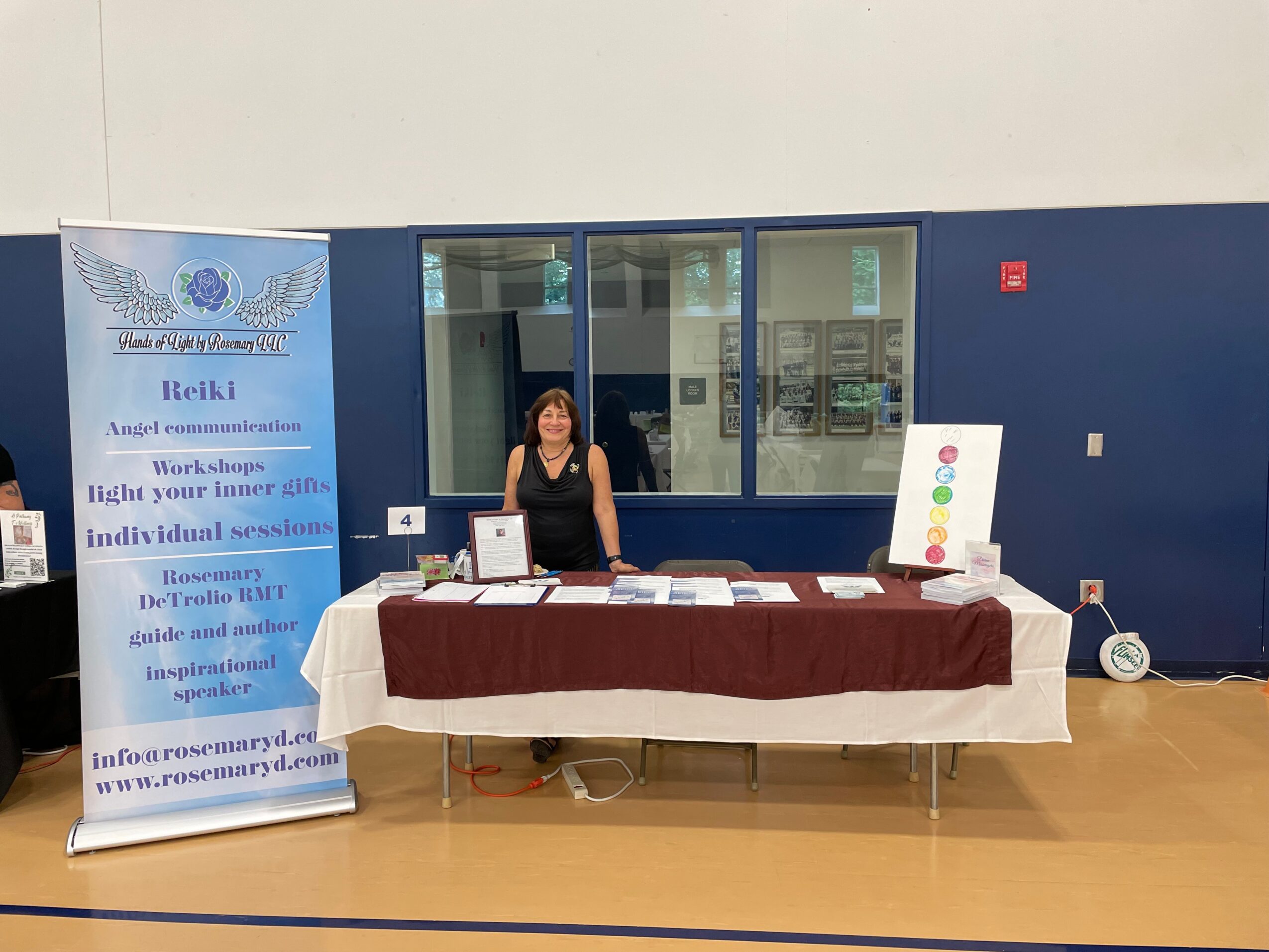 Woman standing behind a table with informational materials, banner on the left, in a room with blue and white walls.