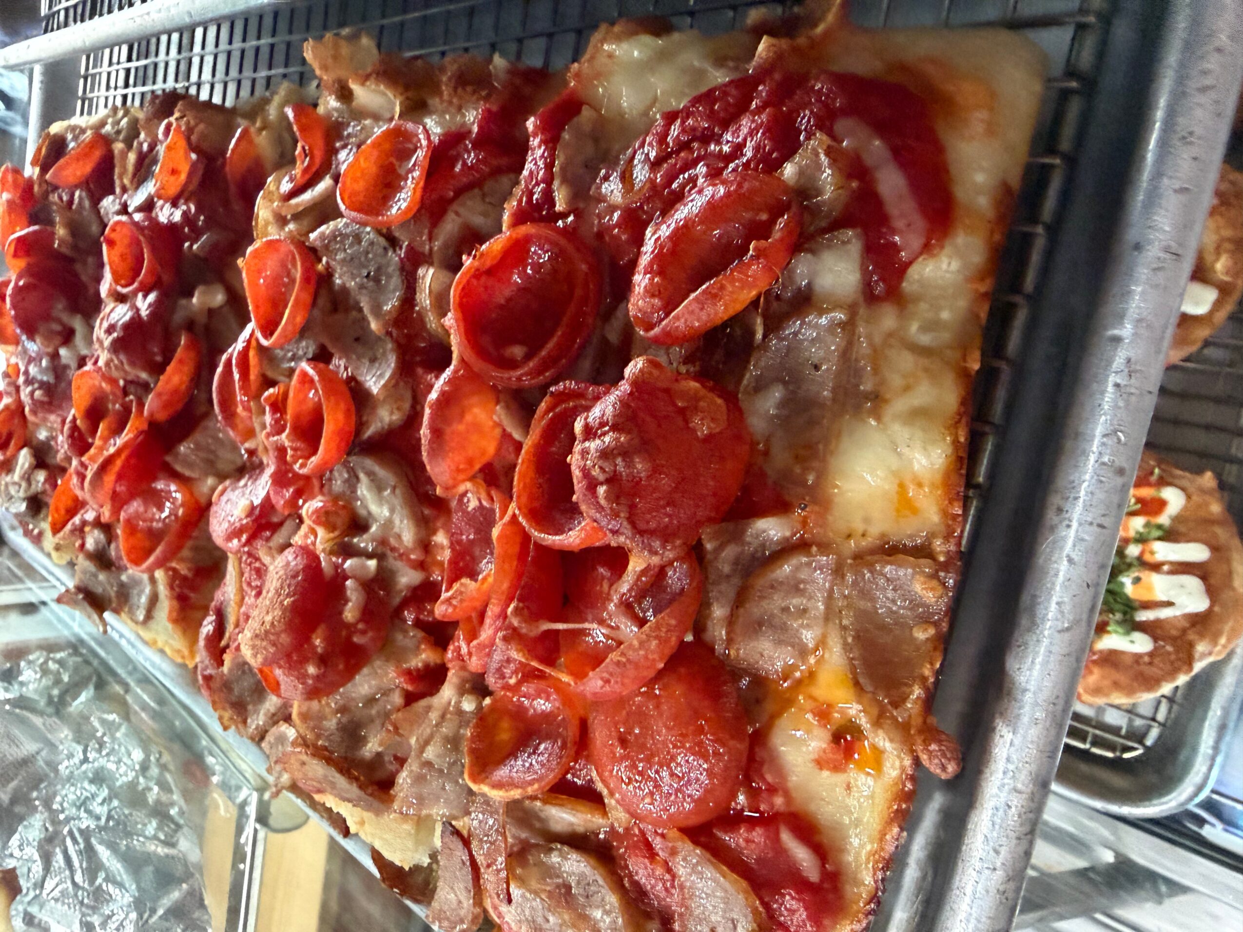 Pizza with pepperoni, sausage, and vegetables on a tray, viewed from the side.