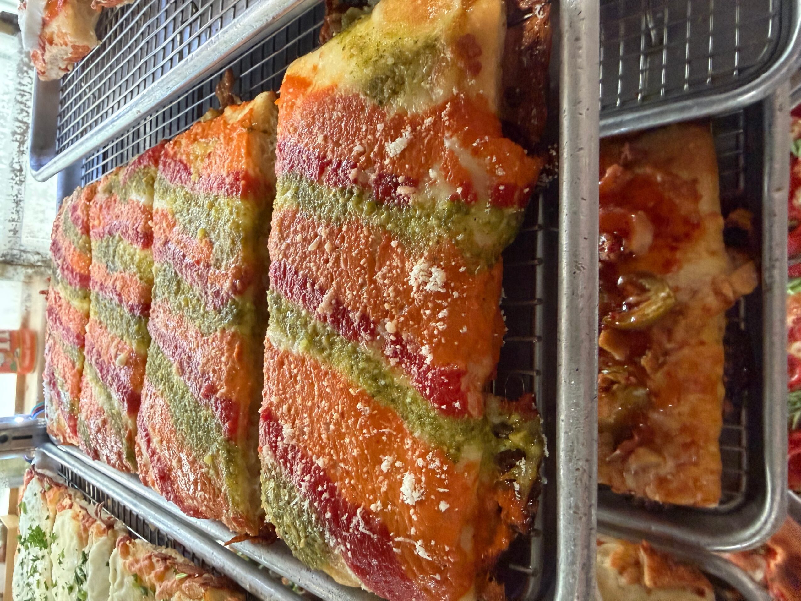 Slices of colorful layered cake with green, pink, and orange layers, topped with white sprinkles, on a tray.