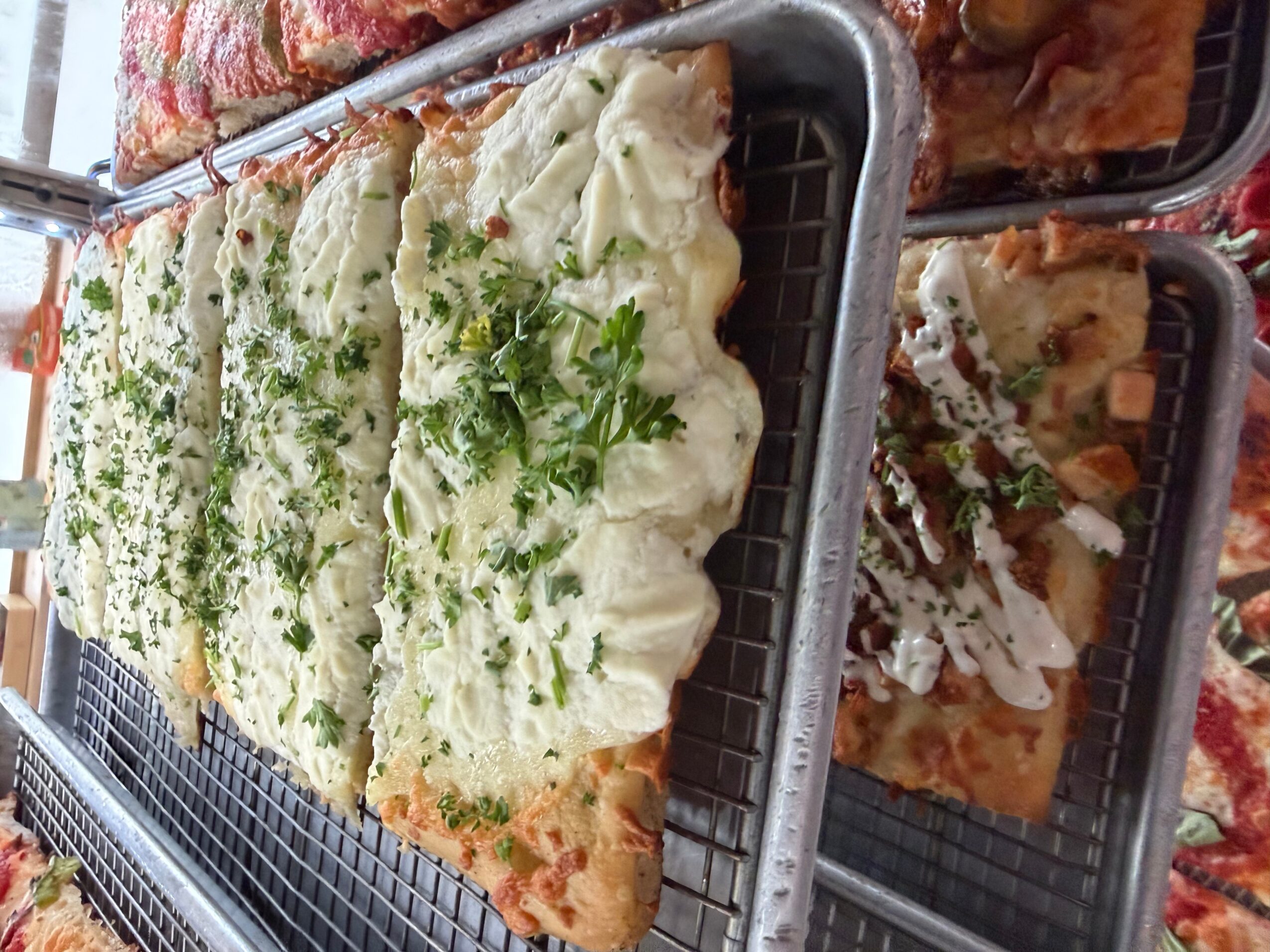 Multiple slices of pizza topped with cheese, herbs, and green garnish on a metal tray.