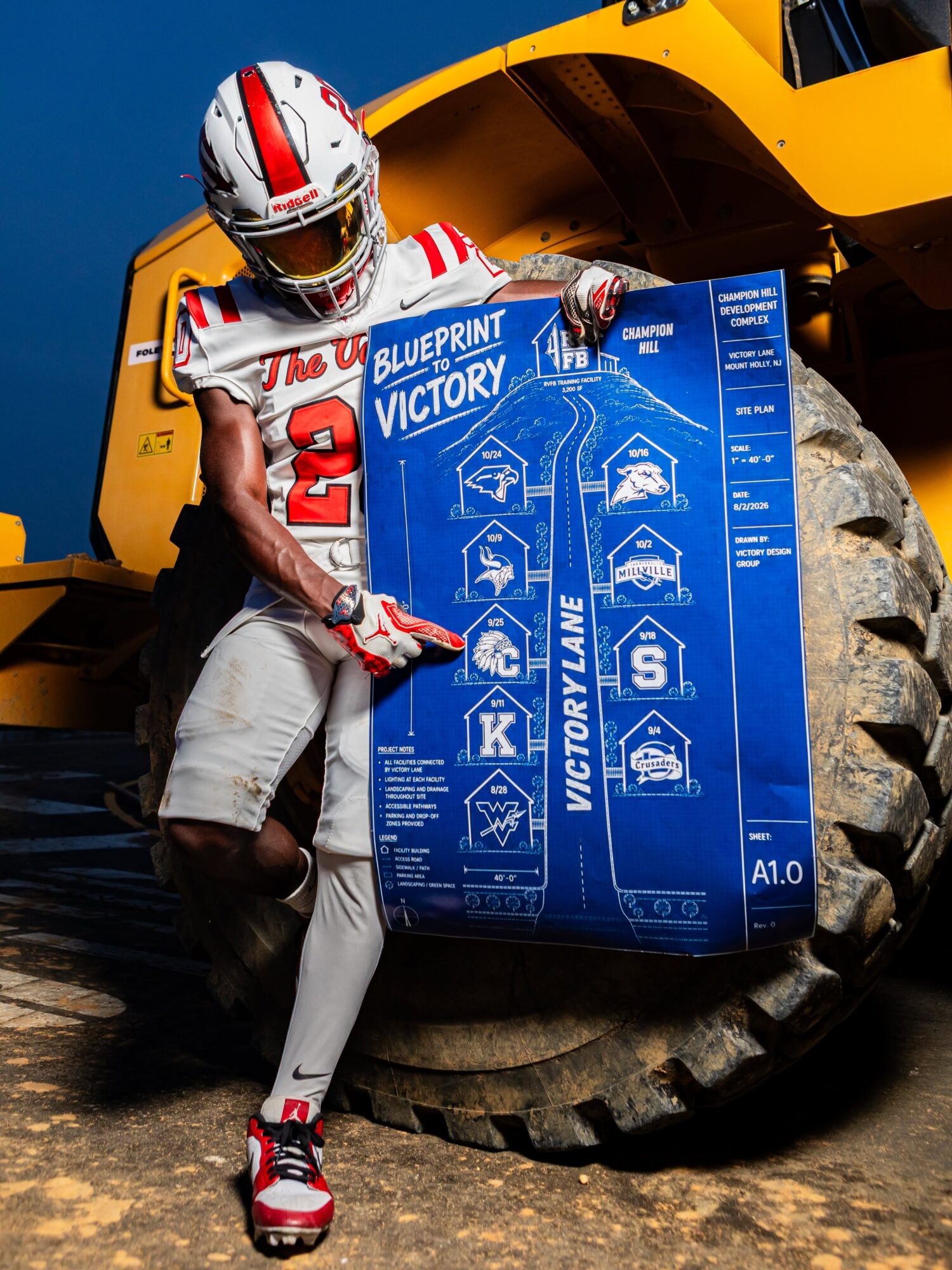 Person in racing gear holding a large blueprint with construction vehicle in background.