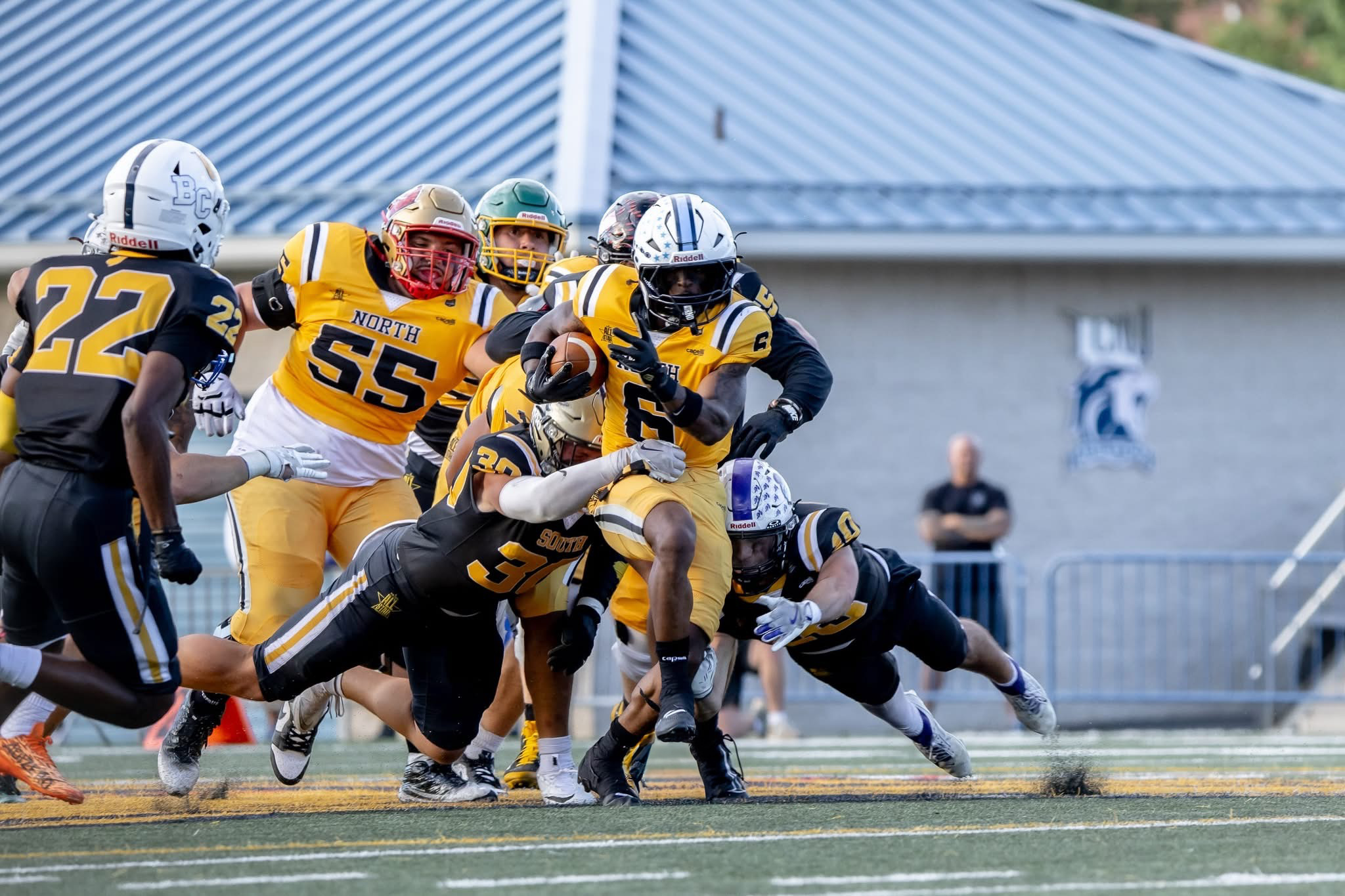 Football players in yellow and black uniforms tackle a player in black and white uniform on the field.