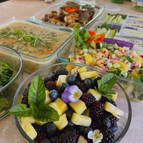 Assorted dishes including a fruit salad with blackberries, blueberries, pineapple, and mint leaves, and other prepared foods on a table.