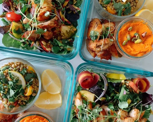 Four containers of colorful salads and dips with vegetables, lemon wedges, and garnishes, viewed from above.