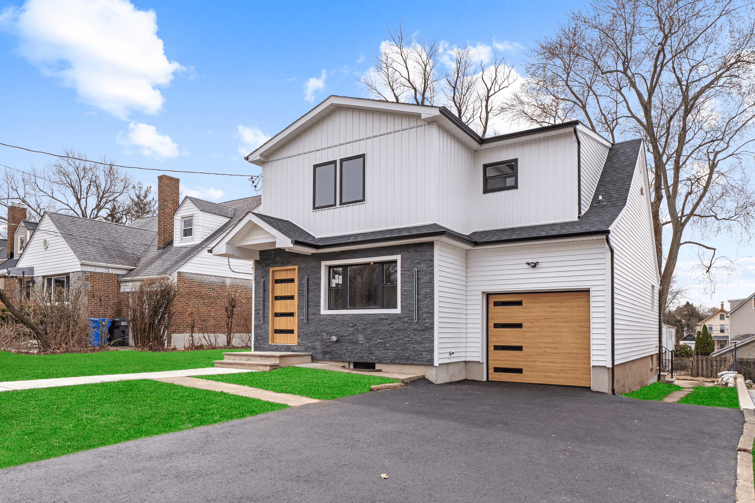 Modern two-story house with white and black exterior, garage door, and a small front yard with green grass.