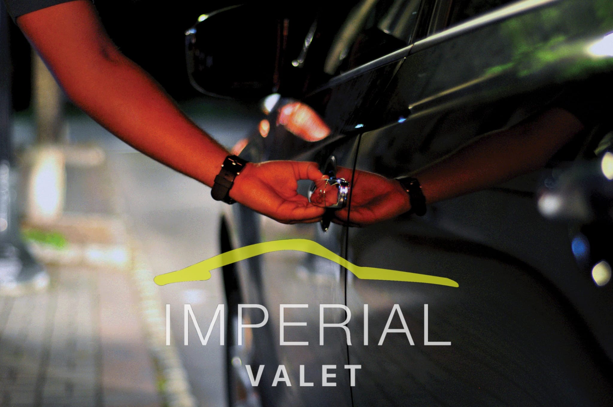 Person's hand holding car keys near a black car door, with text 'IMPERIAL VALET' below.