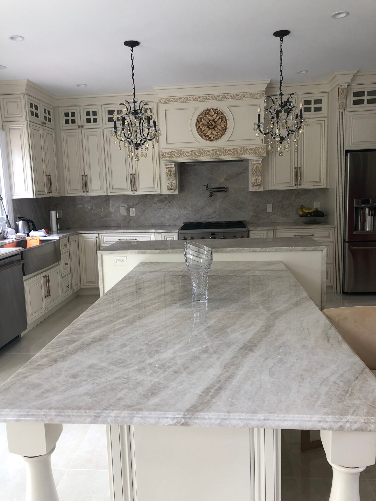 Upright view of a kitchen with a marble island, white cabinets, and a chandelier, viewed from the side.