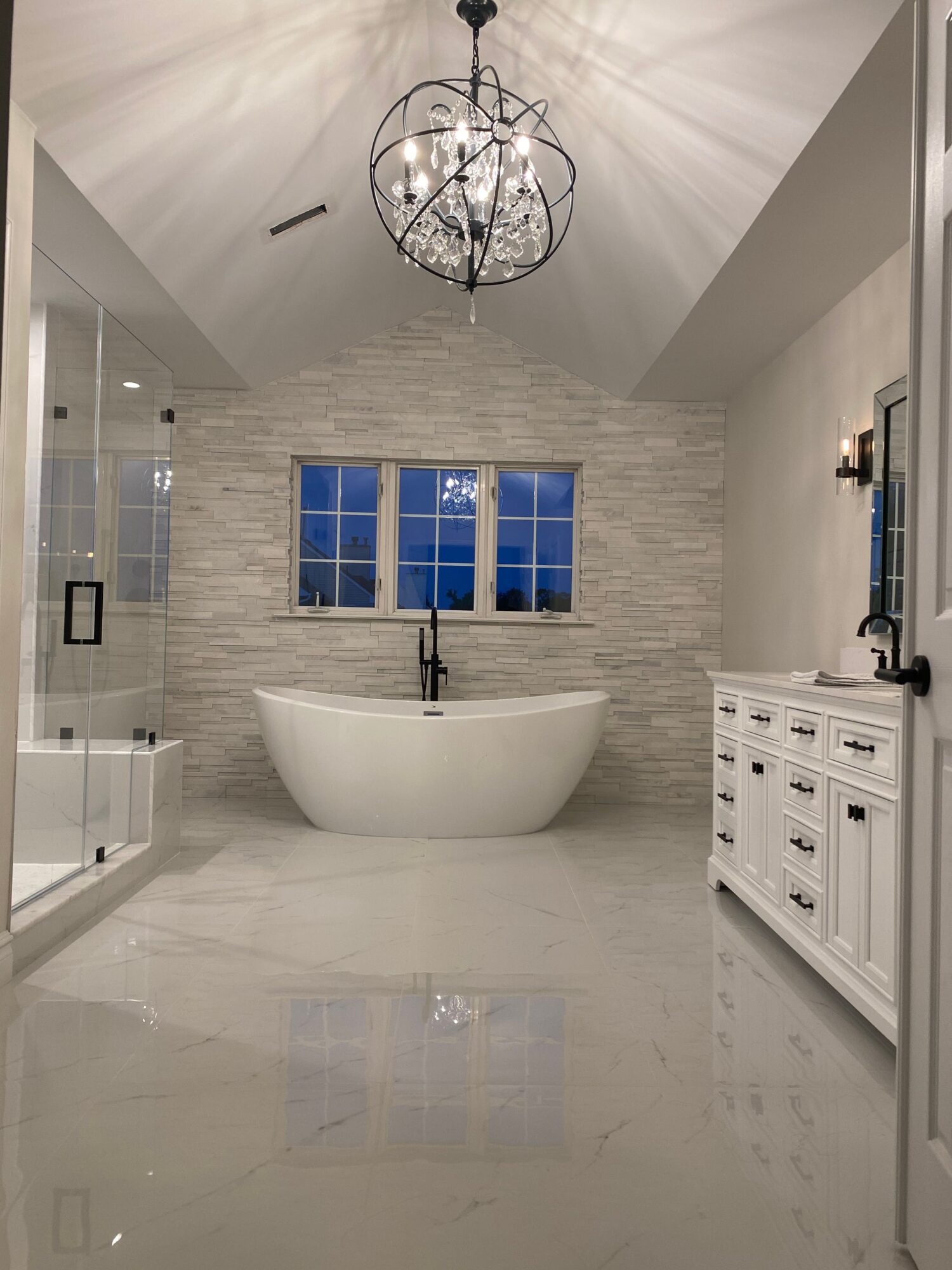 Bathroom with a freestanding bathtub, window, textured wall, and chandelier, viewed from the doorway.