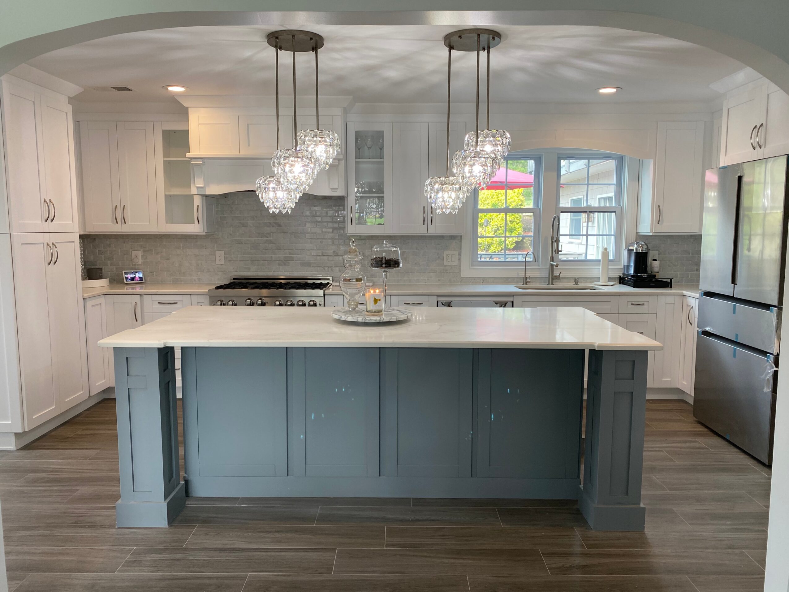 Modern kitchen with white cabinets, a large island with a blue base, pendant lights, and stainless steel appliances.