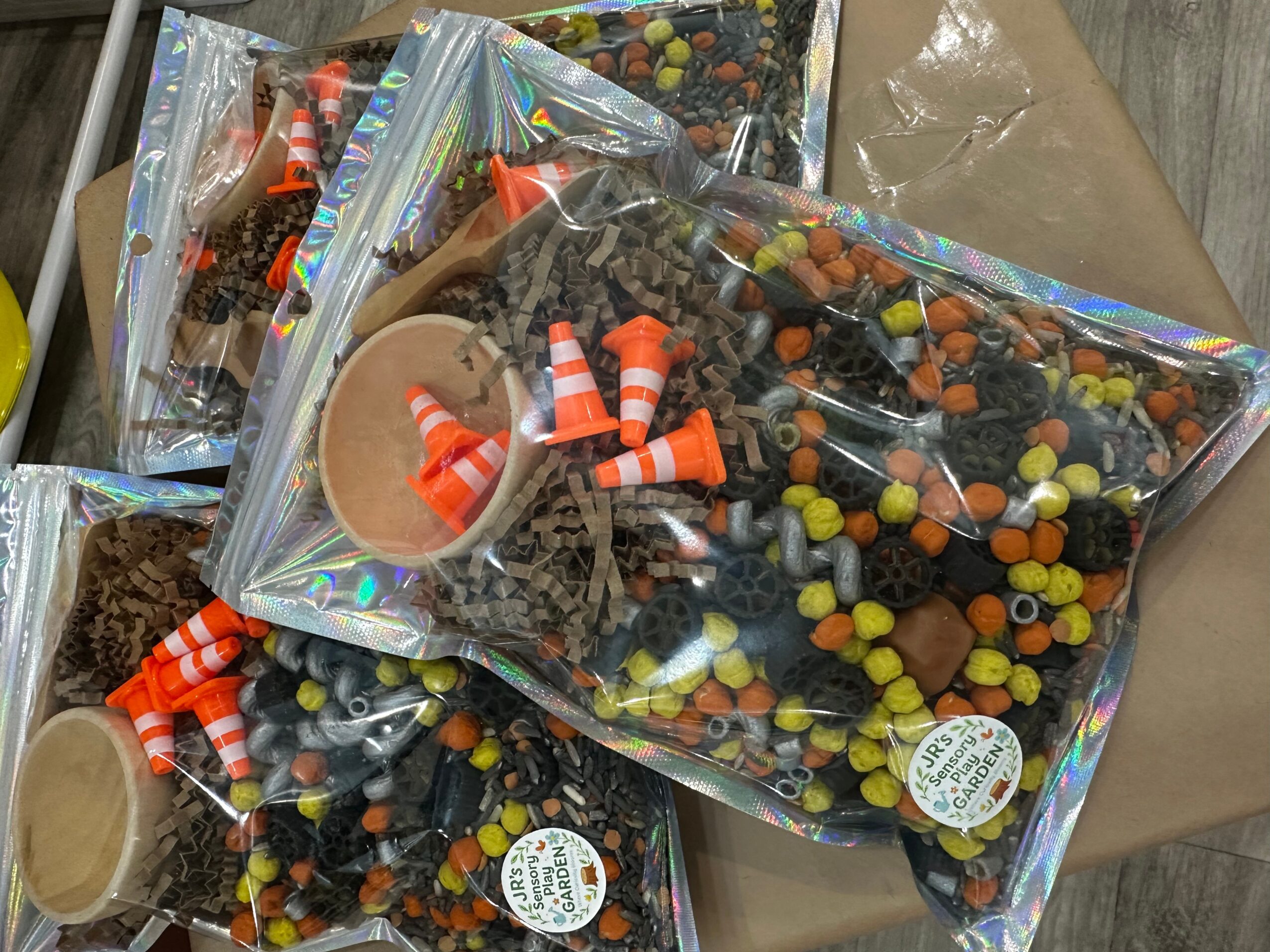 Multiple clear plastic bags filled with colorful small candies and orange and white striped candy canes, on a table.