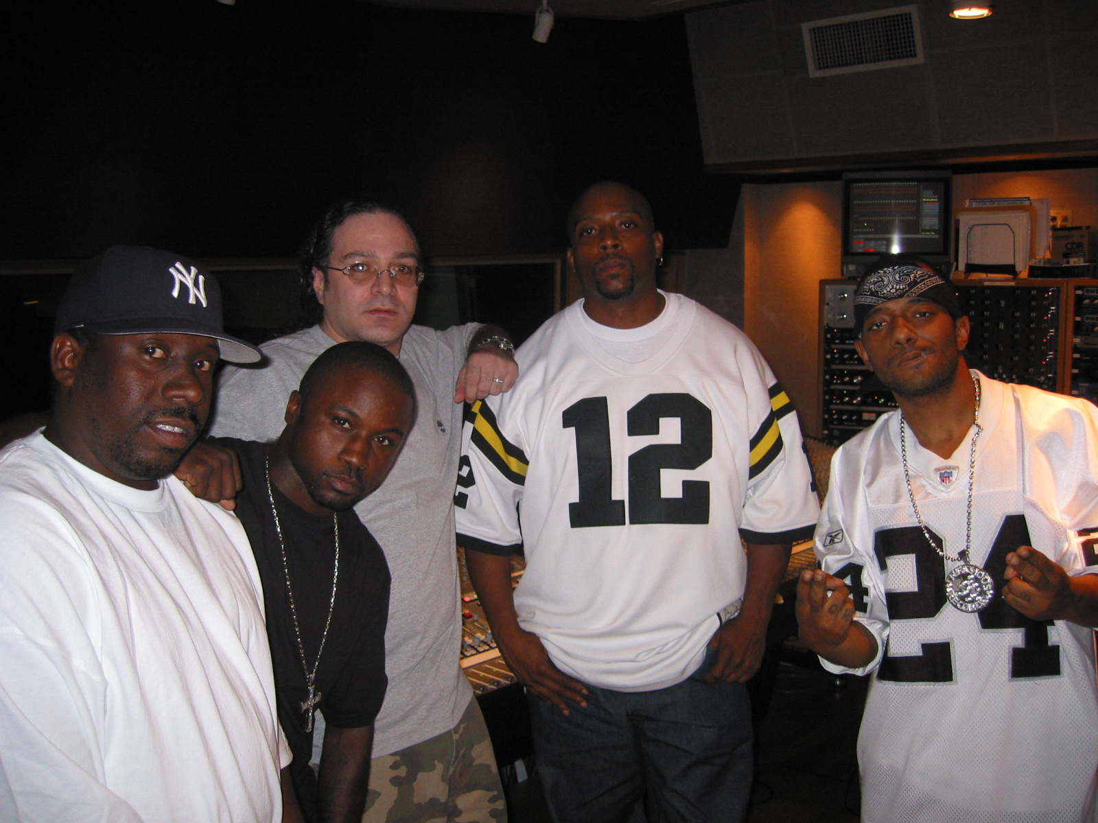 Group of five men standing indoors, some wearing sports jerseys and casual clothing, posing for a photo.