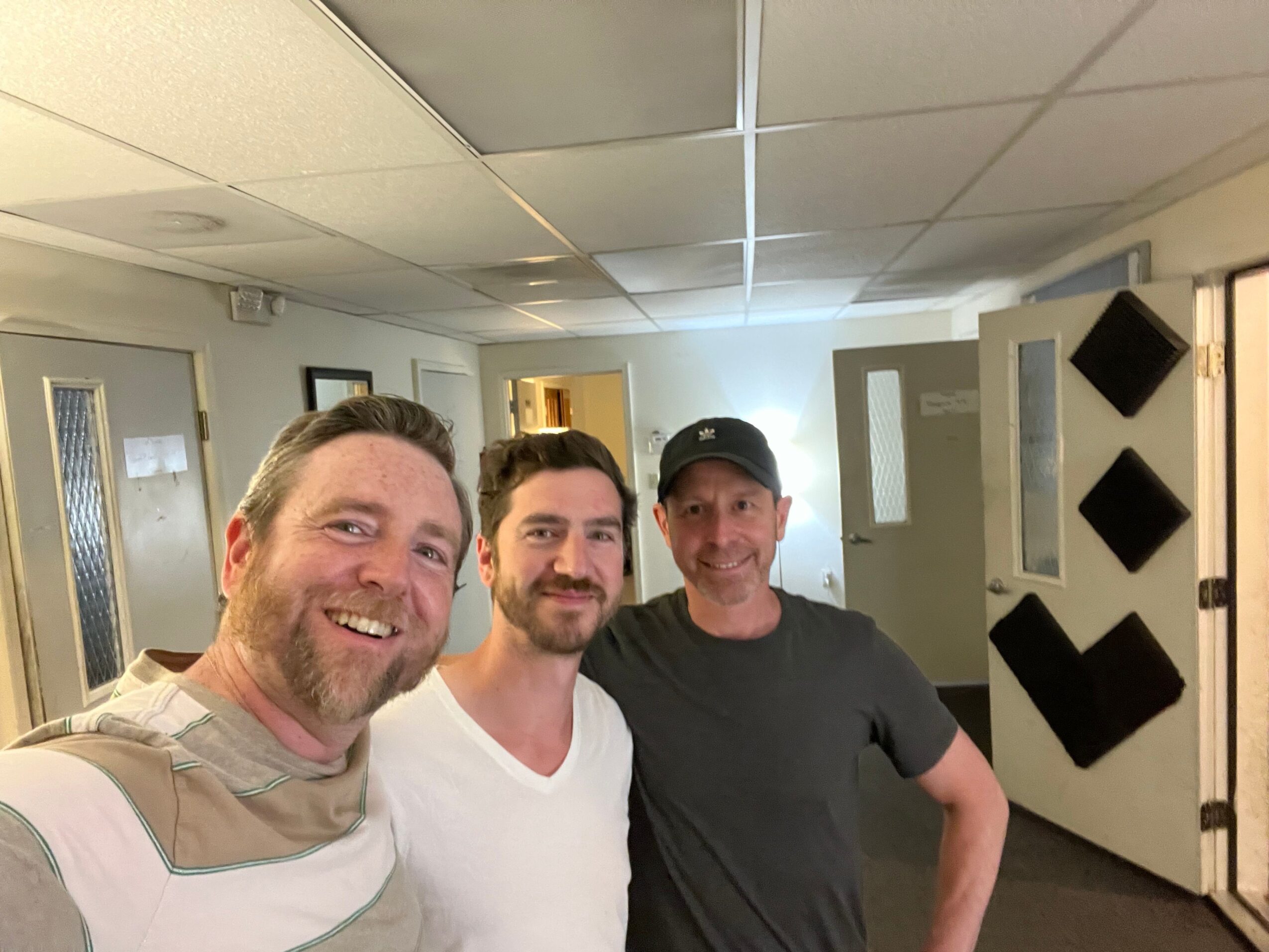 Three people smiling and posing for a photo in an indoor setting with ceiling lights and tiled walls.