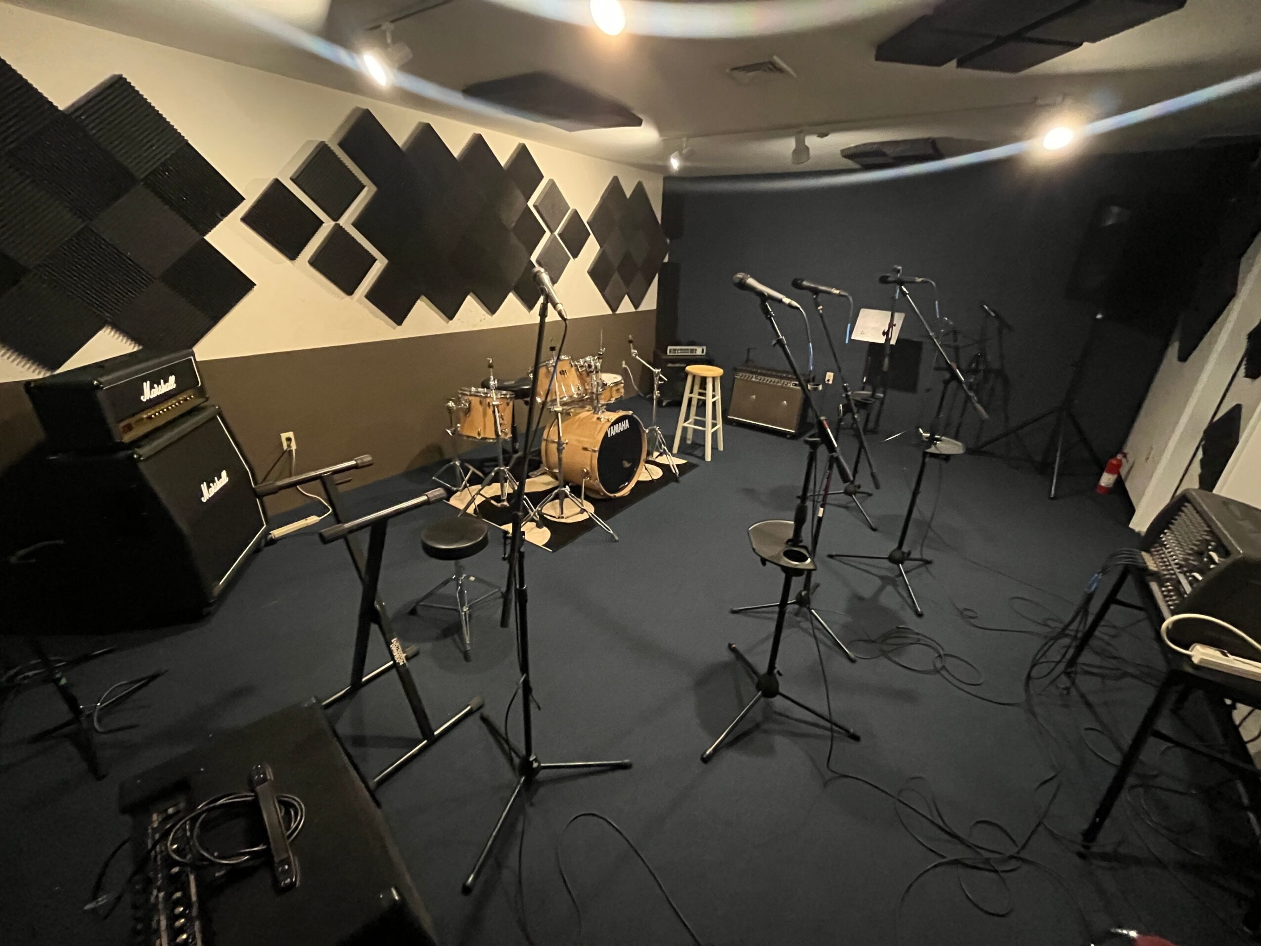 Music rehearsal room with drums, microphones, and amplifiers, and acoustic panels on the wall.