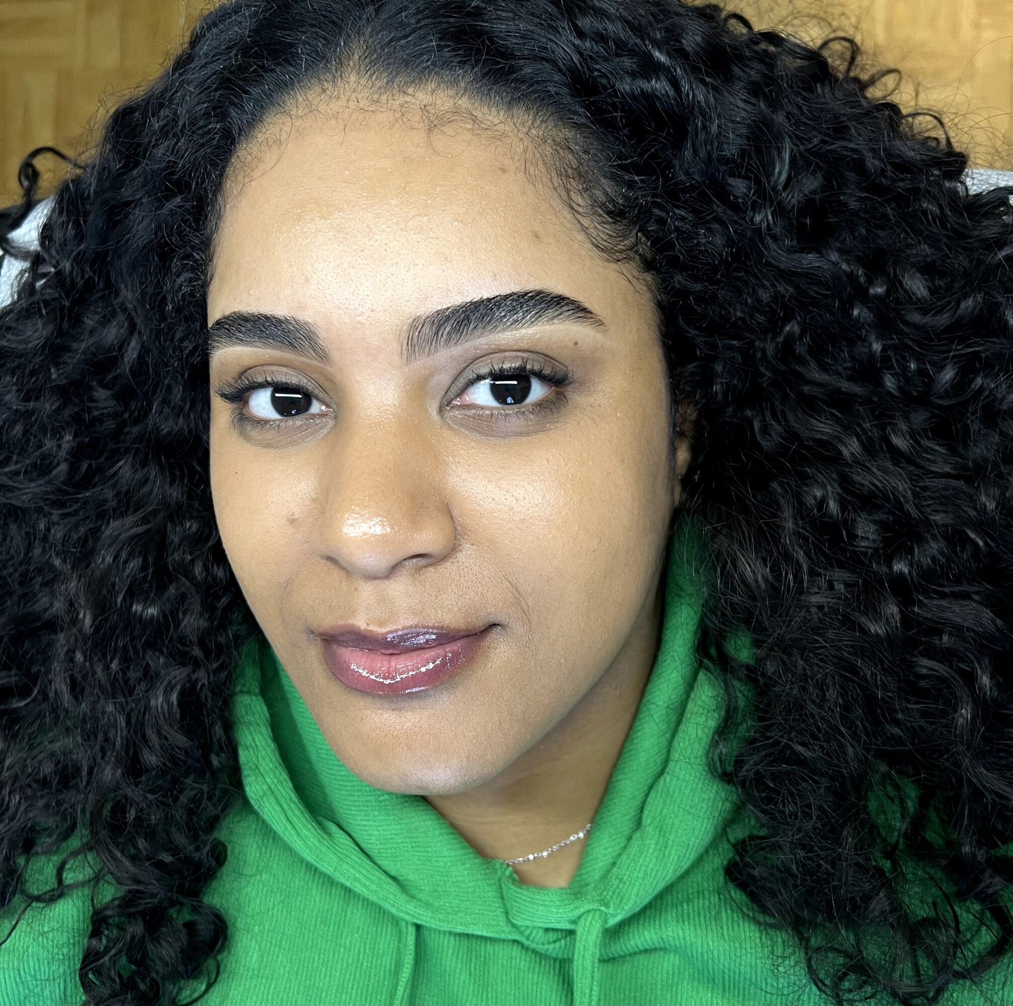 Close-up of a woman with curly hair wearing a green hoodie, smiling slightly, with a neutral background.