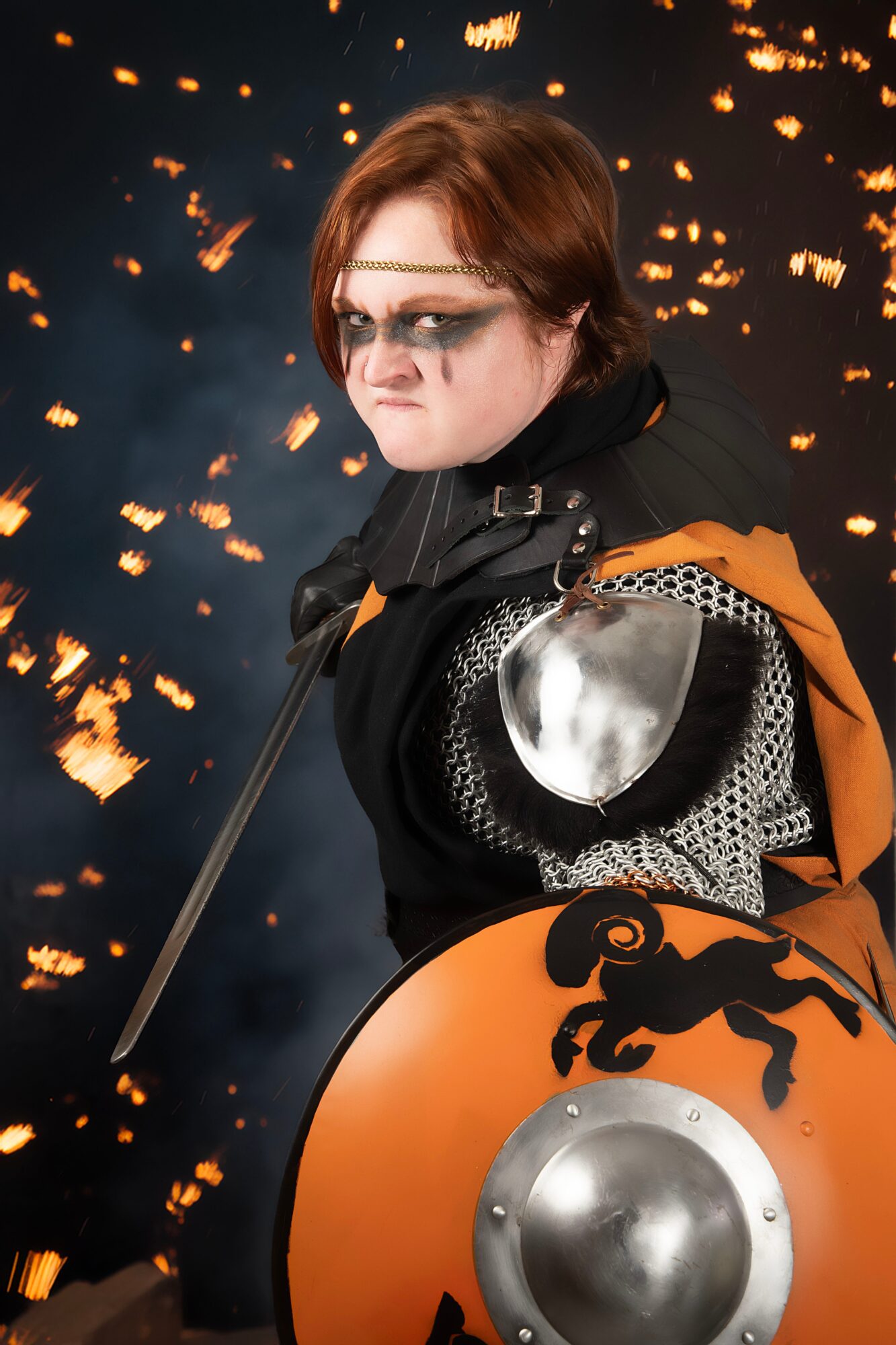 Person dressed as a medieval warrior with armor, shield, and sword, standing against a fiery background.