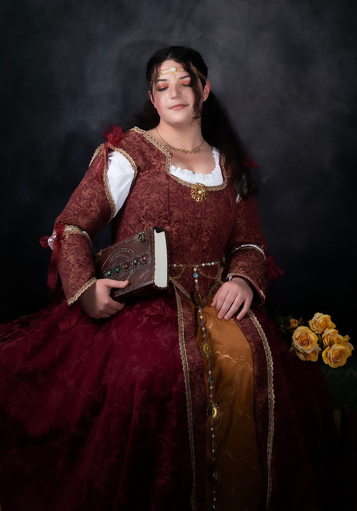 Woman in historical costume holding a book, with yellow roses beside her, against a dark background.