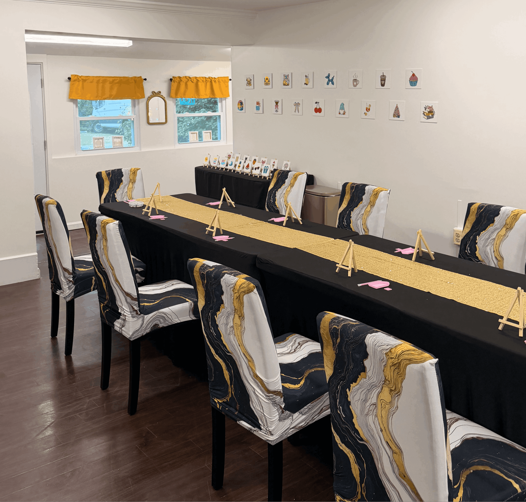 Long table with chairs in a room decorated with artwork on the wall and windows with yellow curtains.