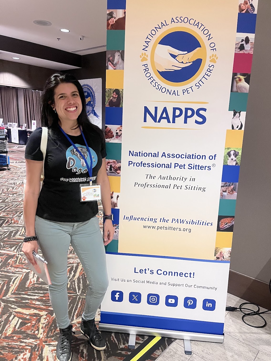 Smiling woman with a backpack standing next to a NABBS banner at a professional event, indoors with carpeted floor.