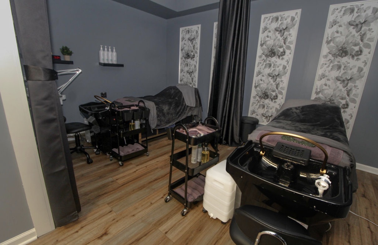 Spa or massage room with massage tables, a black portable grill, and various equipment, with gray walls and wooden floor.
