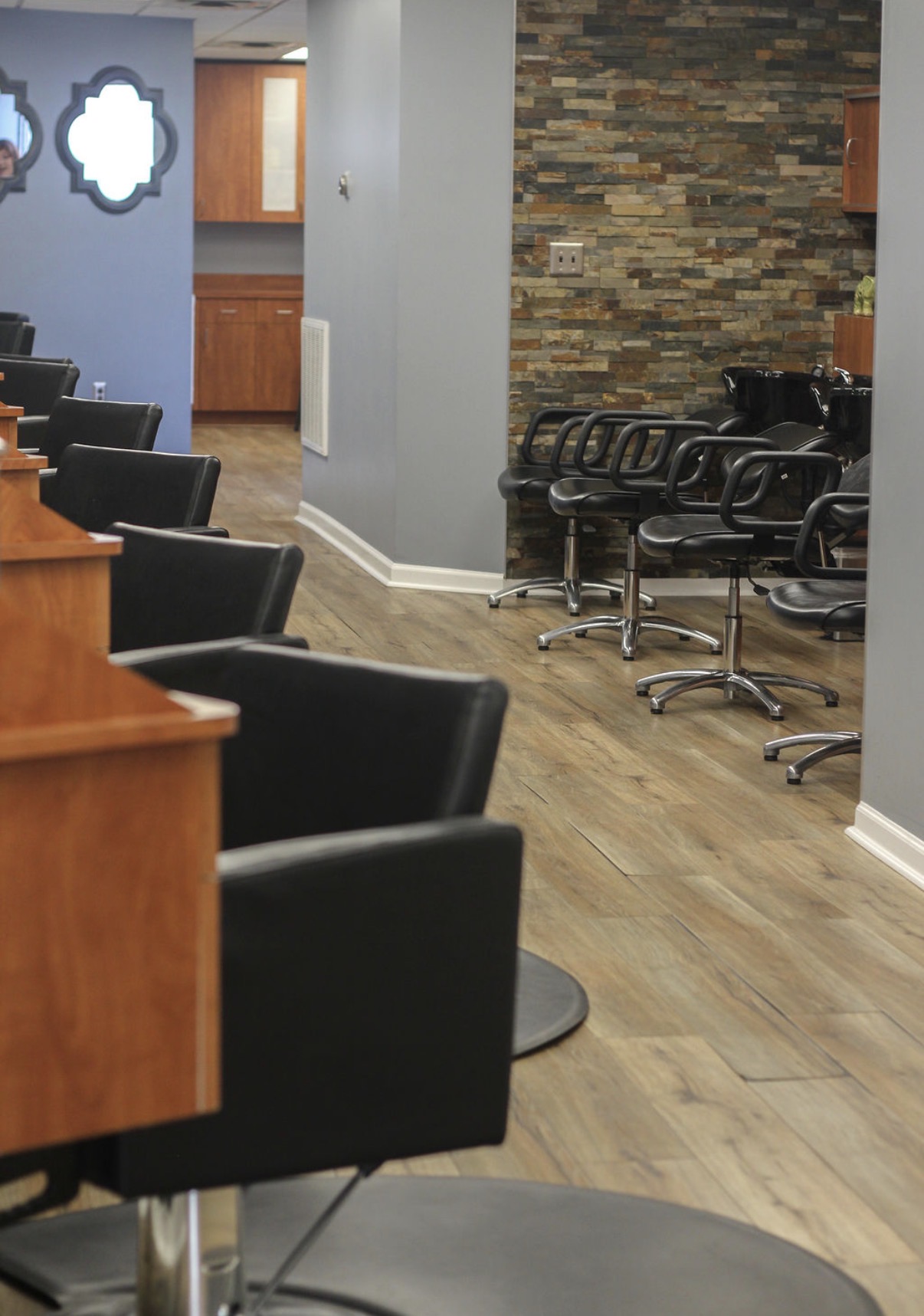 Salon with black chairs, wooden floor, and a stone accent wall, with a doorway and a mirror on the wall.